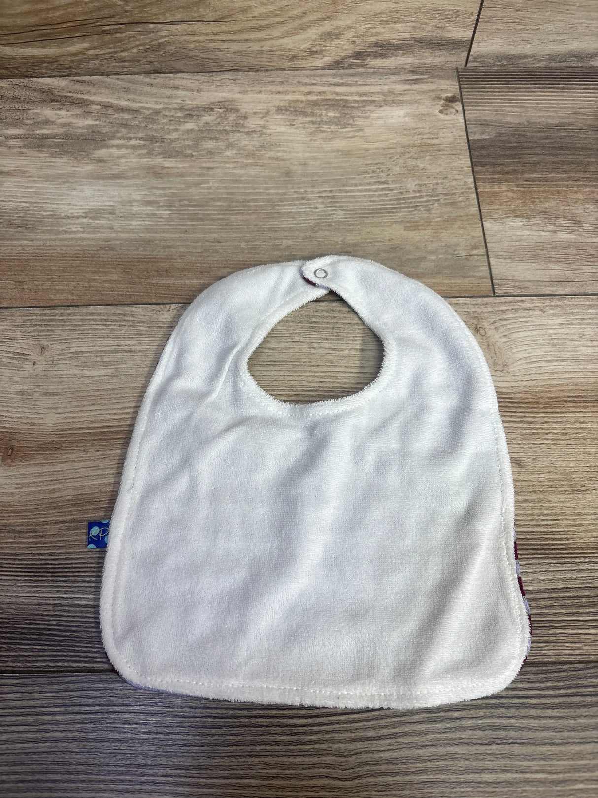 White baby bib with snap closure on wood floor, soft terry cloth fabric for infants