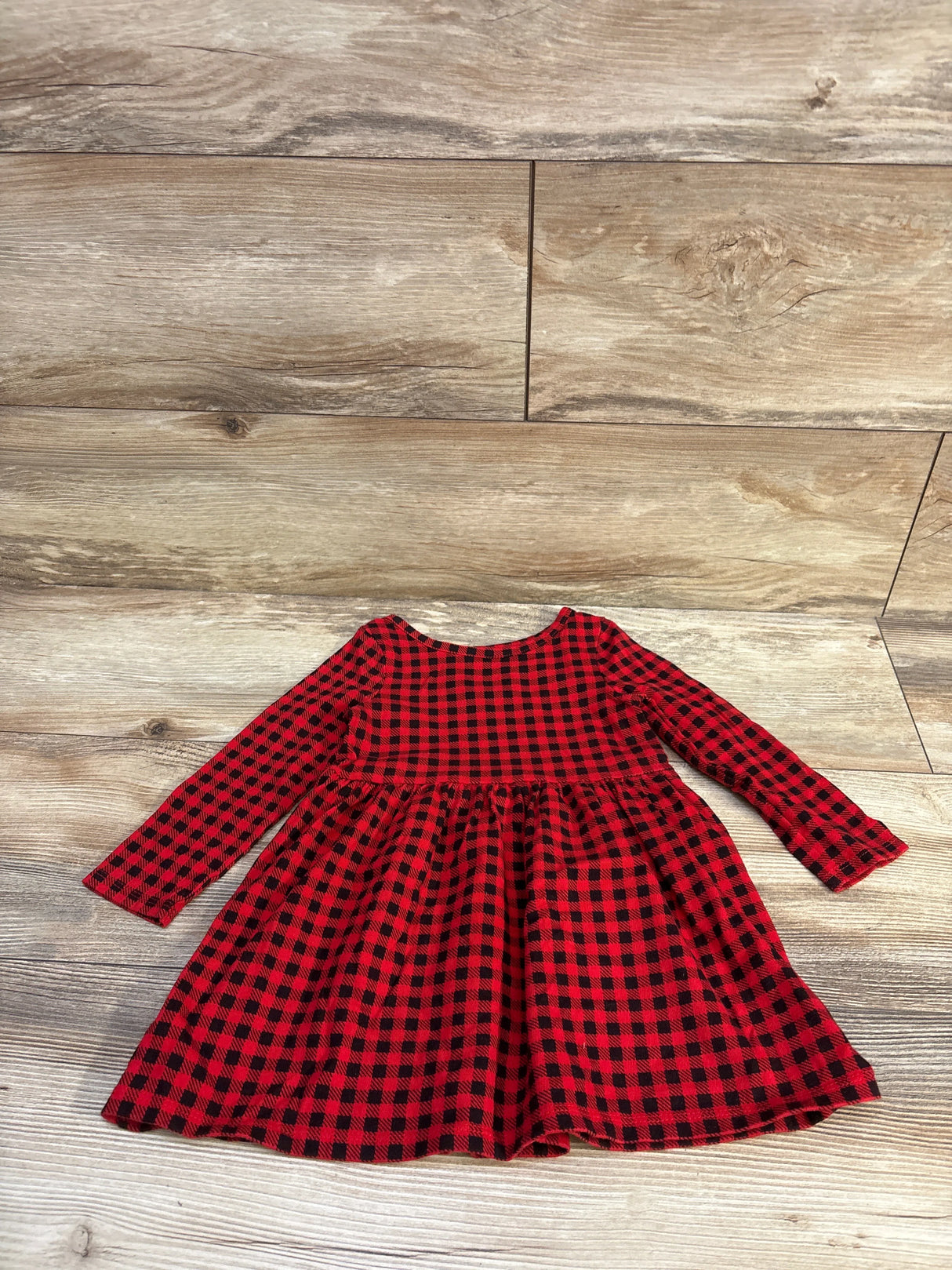 Flat lay of toddler red and black buffalo plaid dress with long sleeves and gathered skirt on wood floor