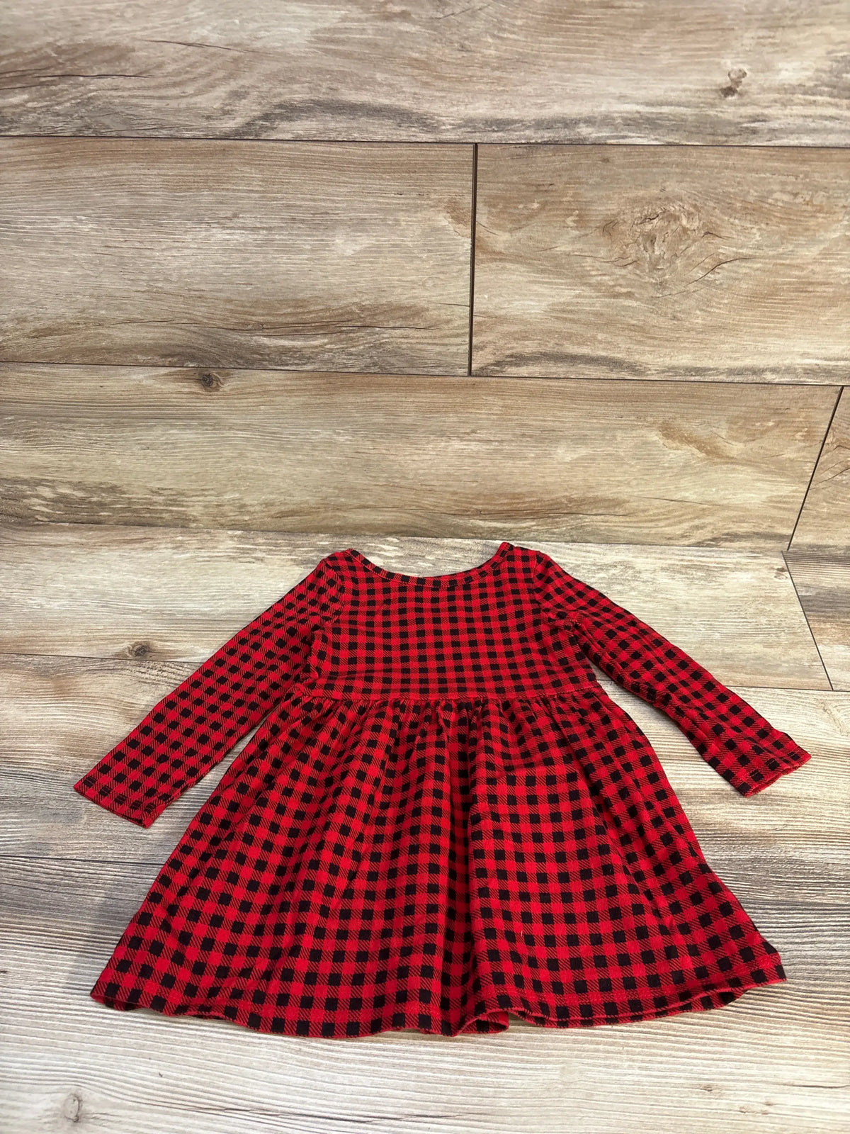 Flat lay of toddler red and black buffalo plaid dress with long sleeves and gathered skirt on wood floor