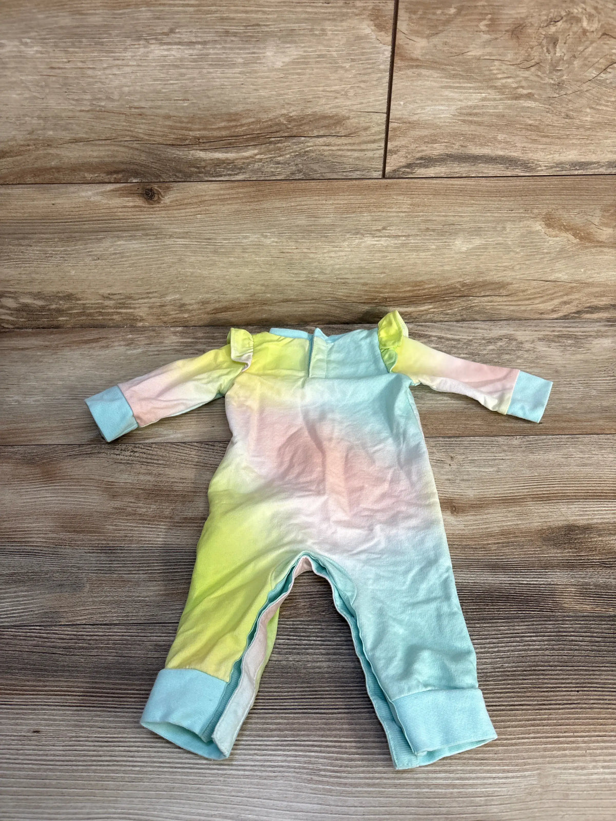 Top down view of baby Hurley coverall in pastel multicolor with long sleeves, ruffled shoulders and snap crotch on wood floor