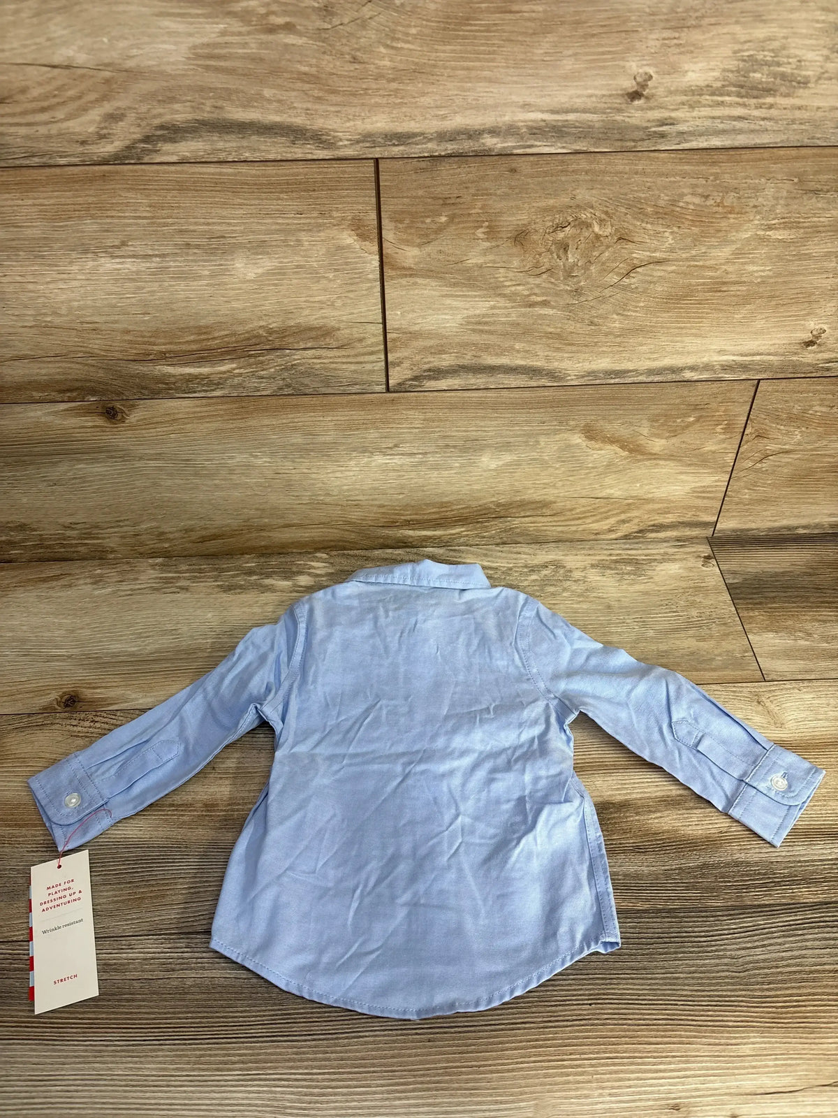 Light blue long-sleeve baby shirt with collar and buttons, laid flat on wooden floor