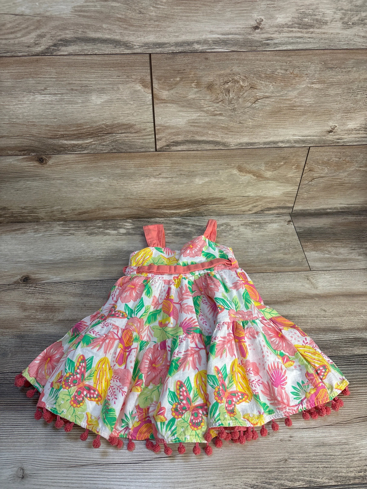 Girls’ sleeveless floral dress with butterfly print and pink pompom trim on wooden floor