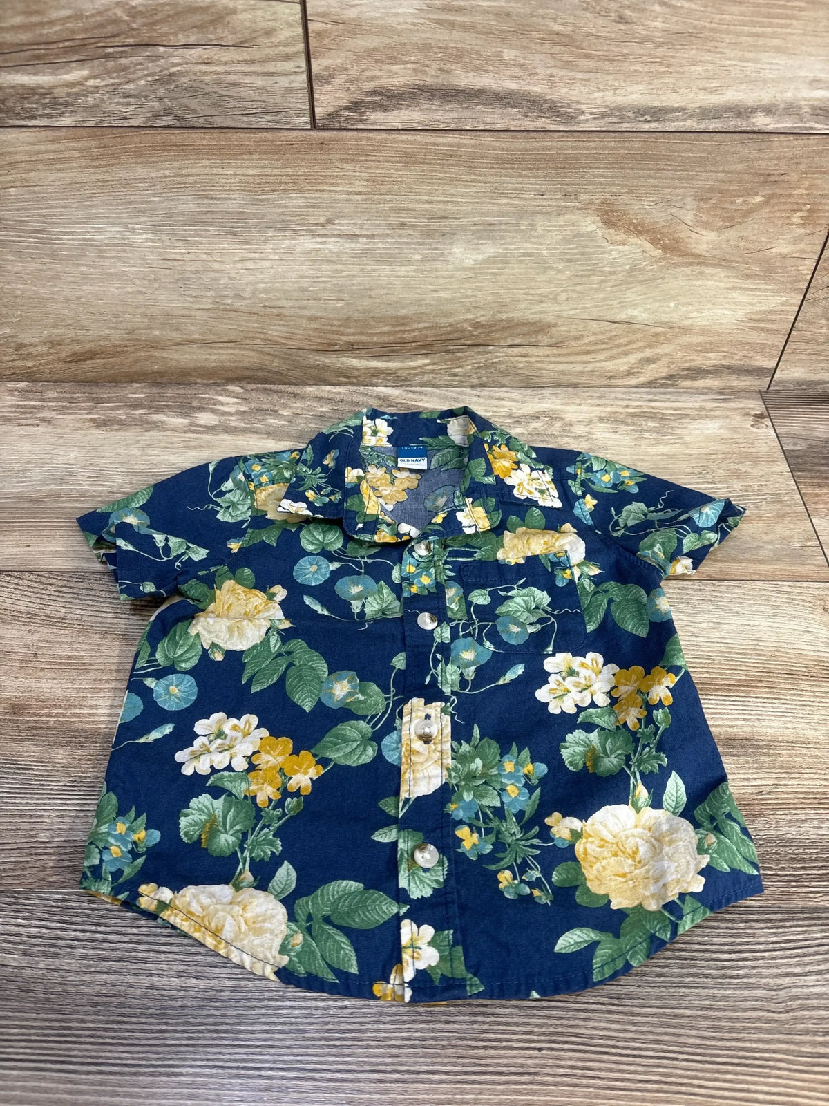 Navy blue short sleeve toddler shirt with yellow and white floral print on wood background