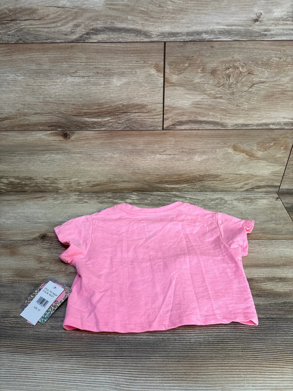 Back view of NWT Freestyle Revolution cat purse shirt in solid pink with hangtag attached on wood plank floor