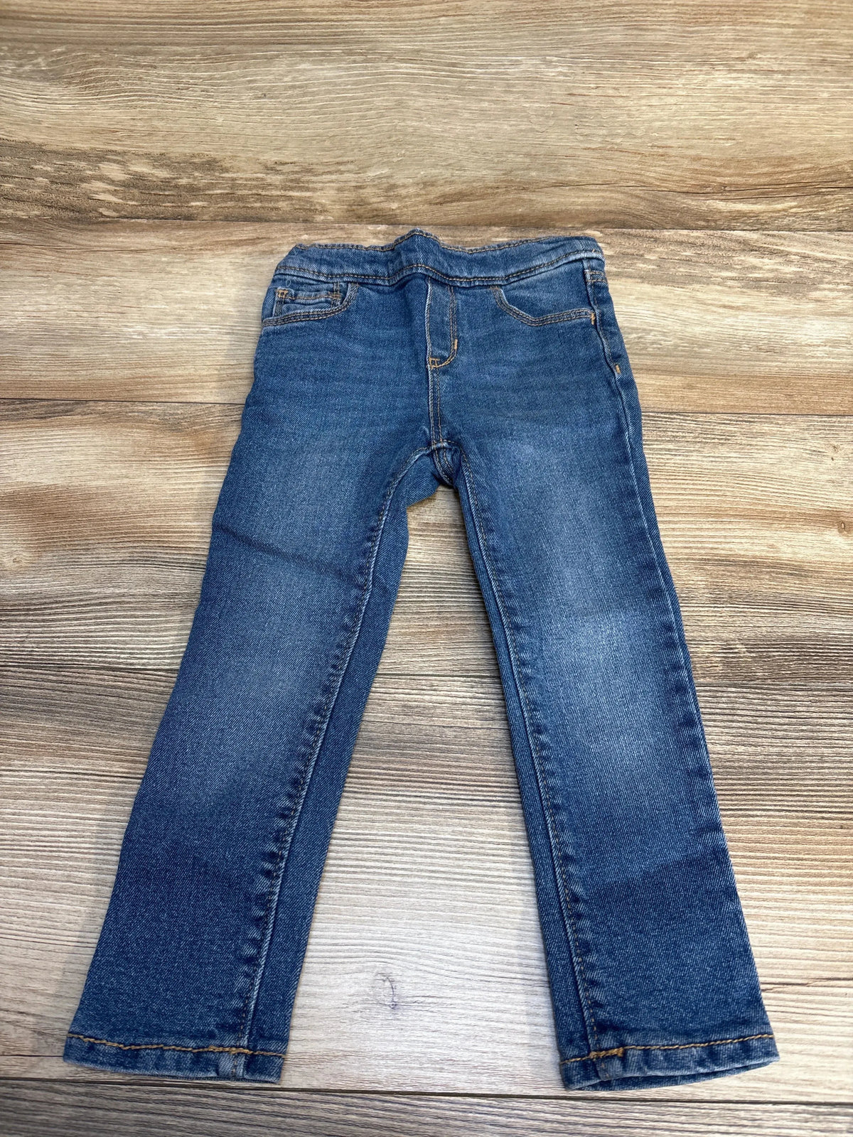 Blue denim kids jeans laid flat on wooden surface, gently used children's clothing