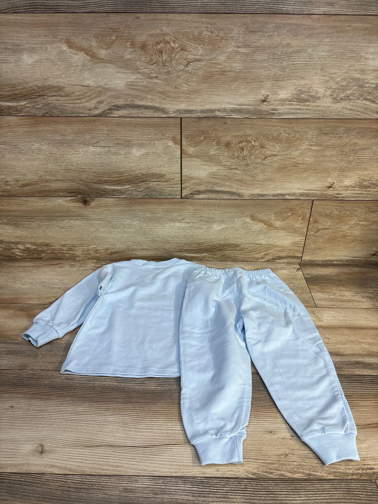 Light blue baby pajama set with long sleeves and elastic cuffs on wood floor