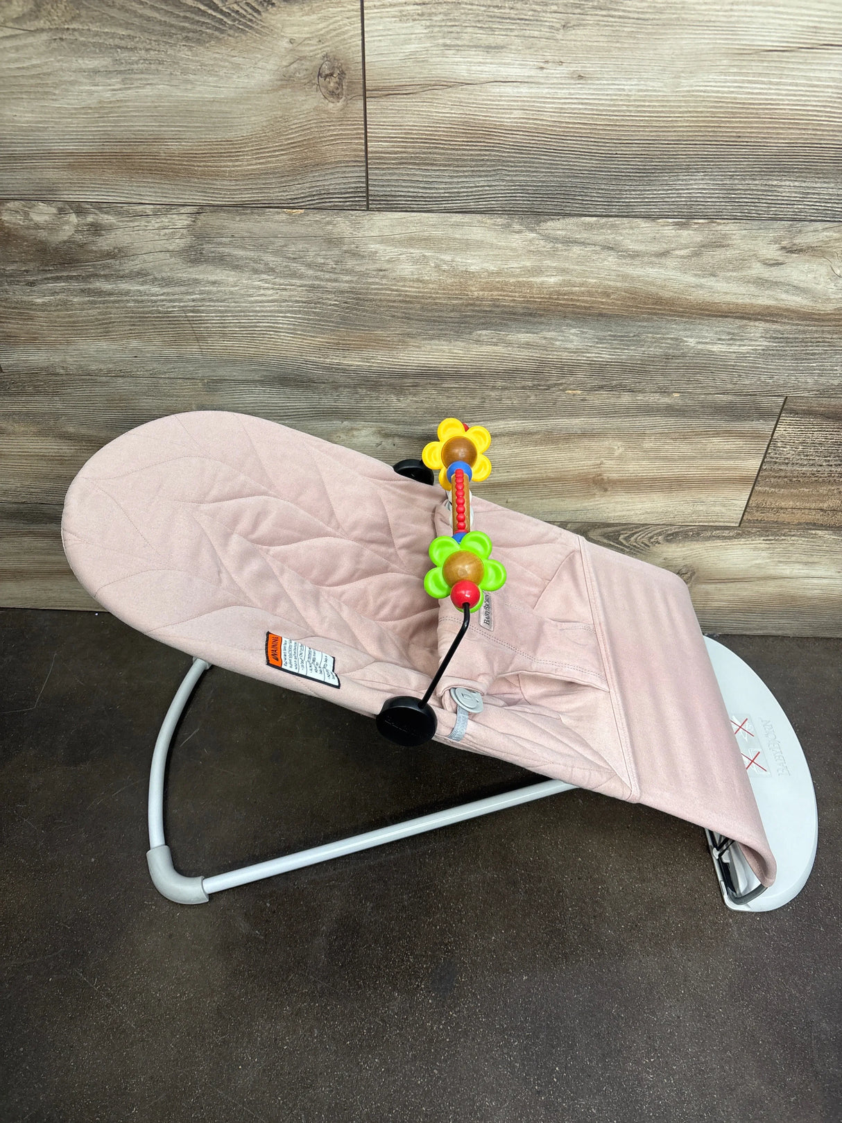 Angled top-down view of Baby Bjorn Bouncer Bliss in dusty pink with quilted petal seat and toy bar on wood background