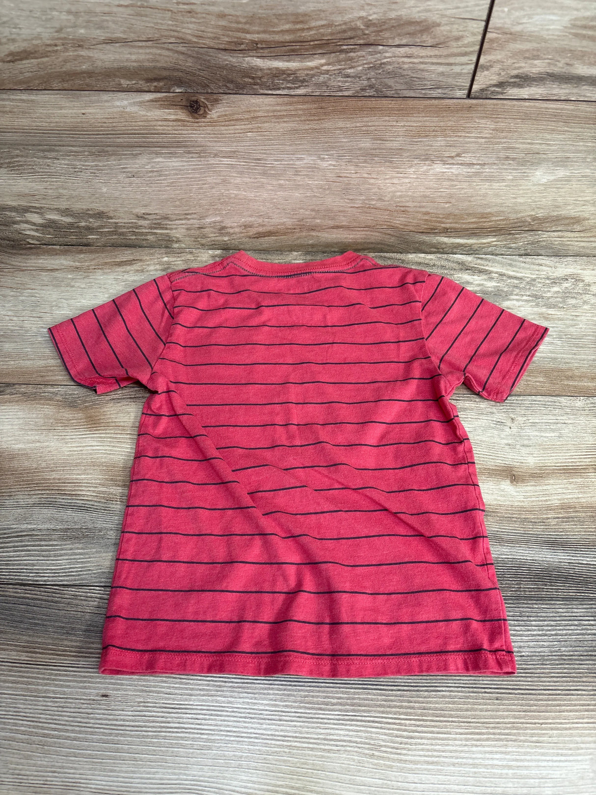 Red short sleeve kids t-shirt with thin black horizontal stripes, laid flat on wood