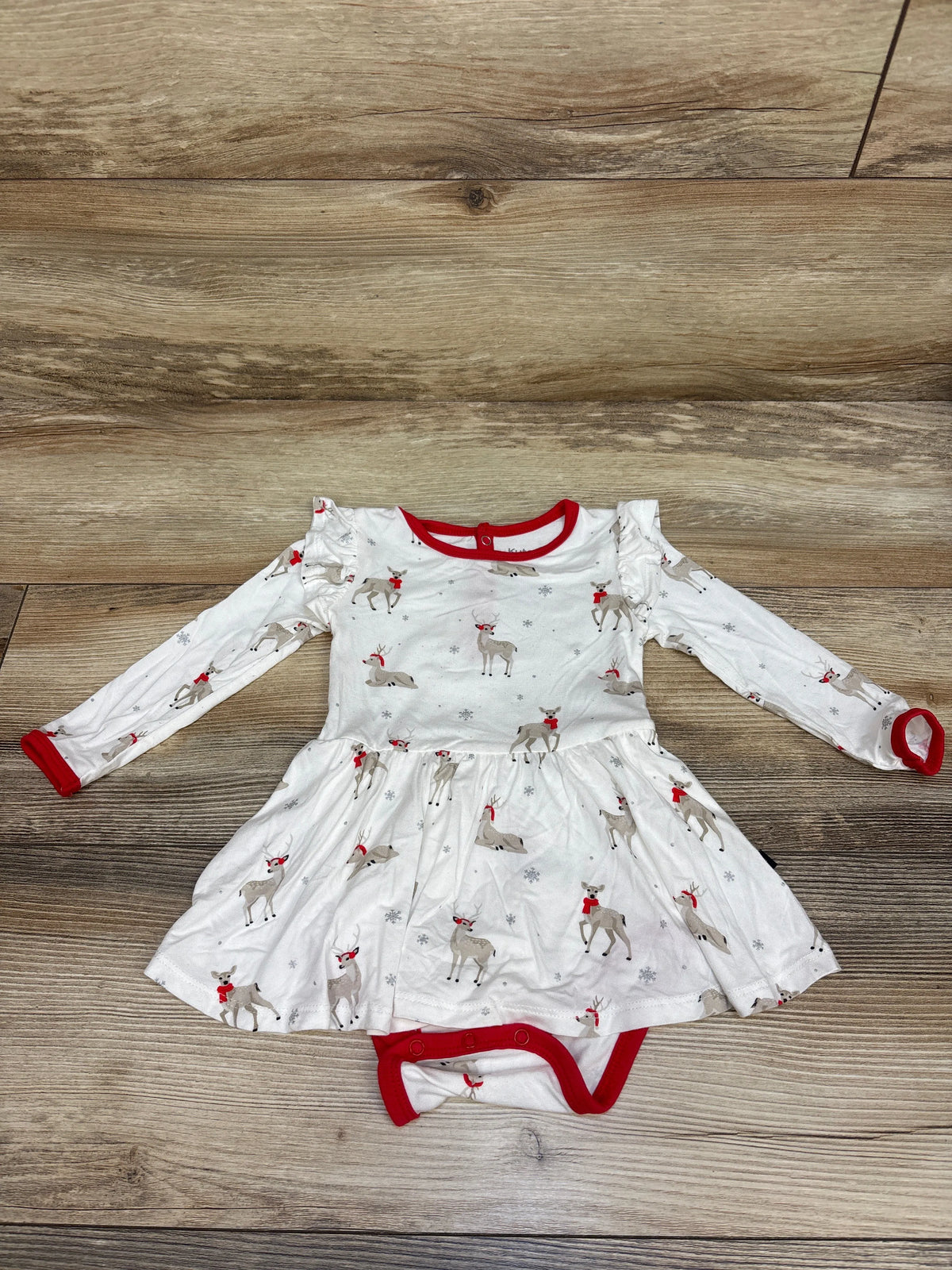 Top-down view of white Kyte Baby Bamboo Cloud Deer Twirl Bodysuit Dress with red trim, deer print, attached bodysuit, and wood background