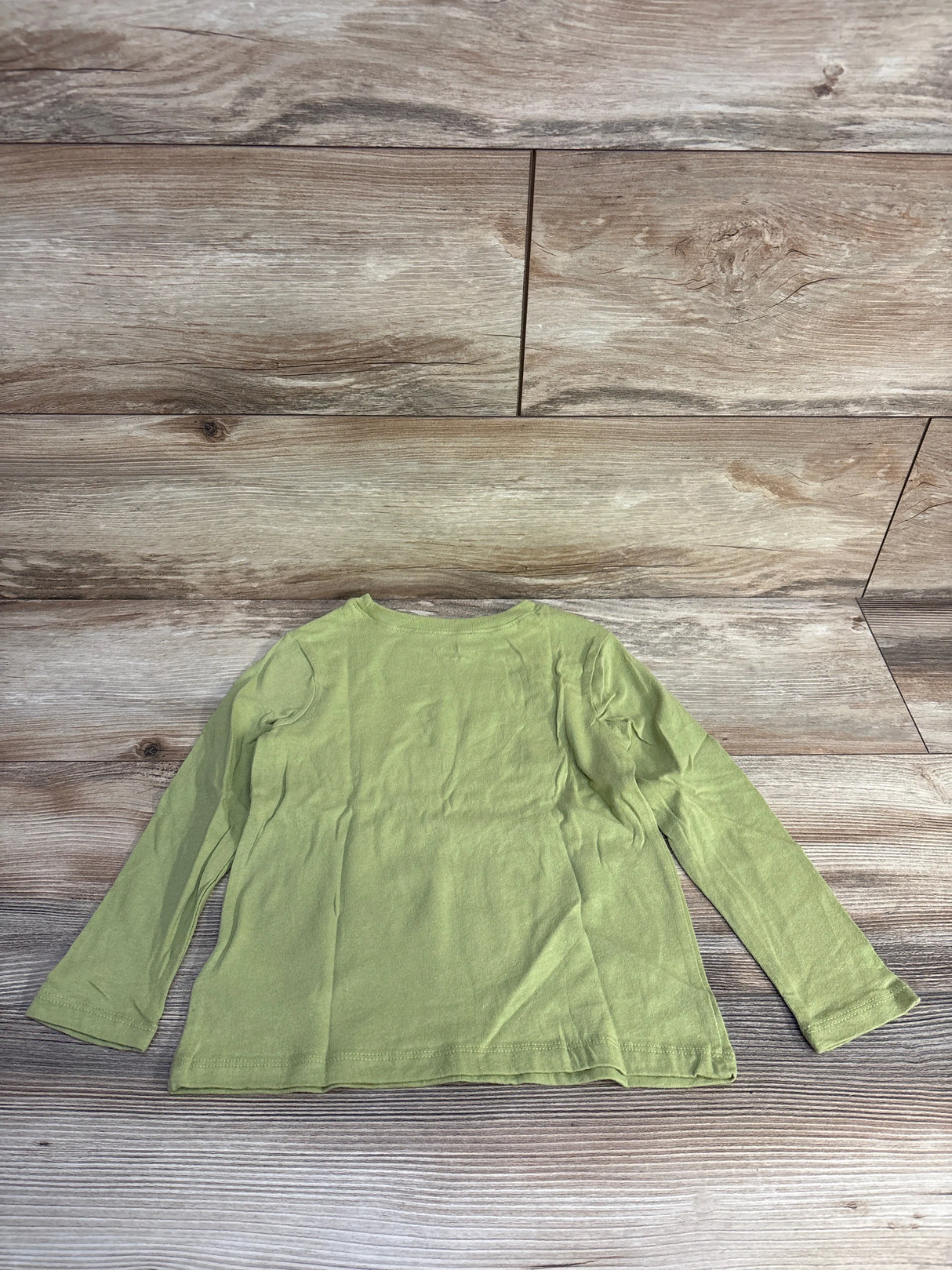 Green long sleeve children's shirt on wood background, flat lay product photo