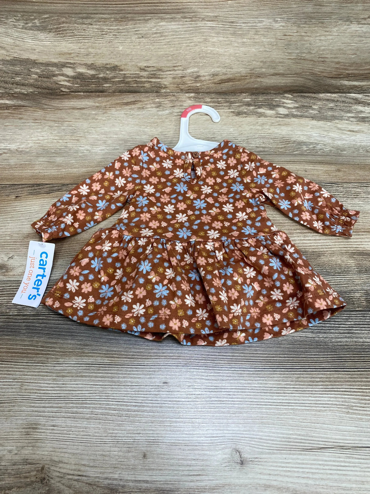 Flat lay of newborn floral dress and matching bloomers showcasing rust brown fabric with pink and blue flowers on wood background