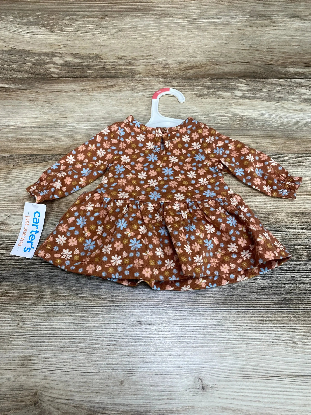Flat lay of newborn floral dress and matching bloomers showcasing rust brown fabric with pink and blue flowers on wood background