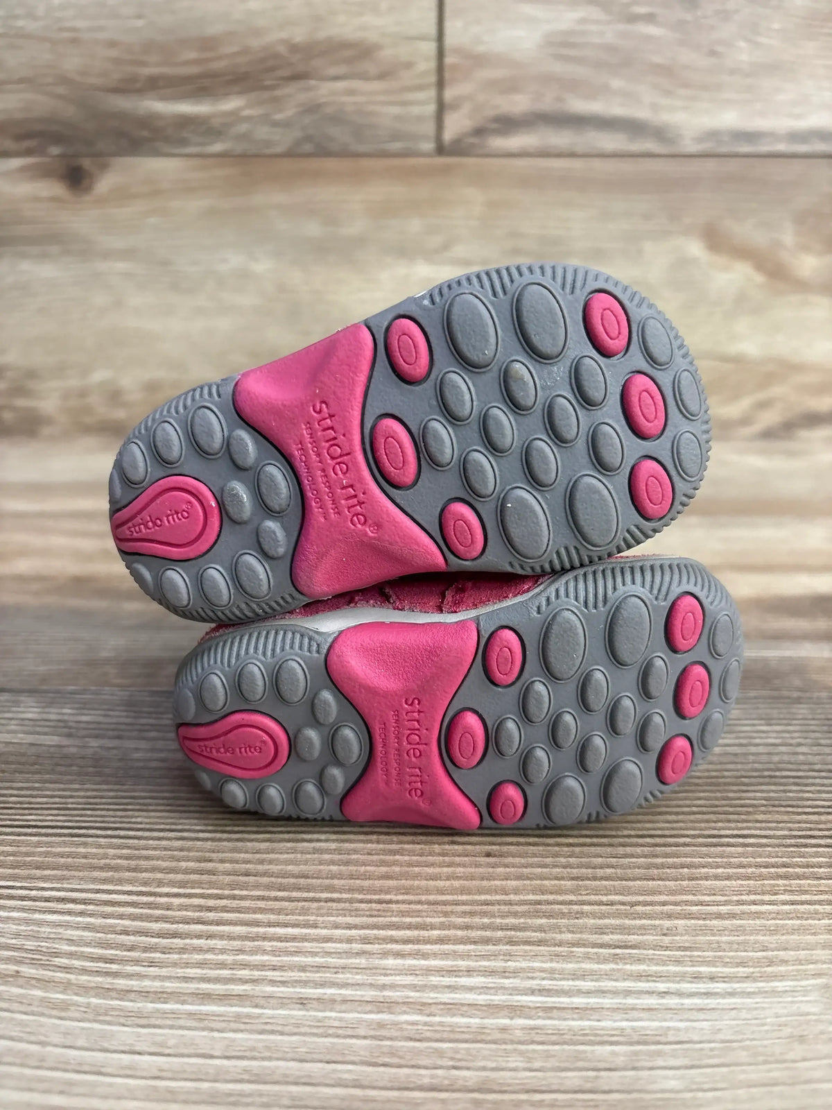 Close-up of Stride Rite SRT Zoe ankle boot soles in pink and gray showcasing rubber grip dot pattern on wood plank floor