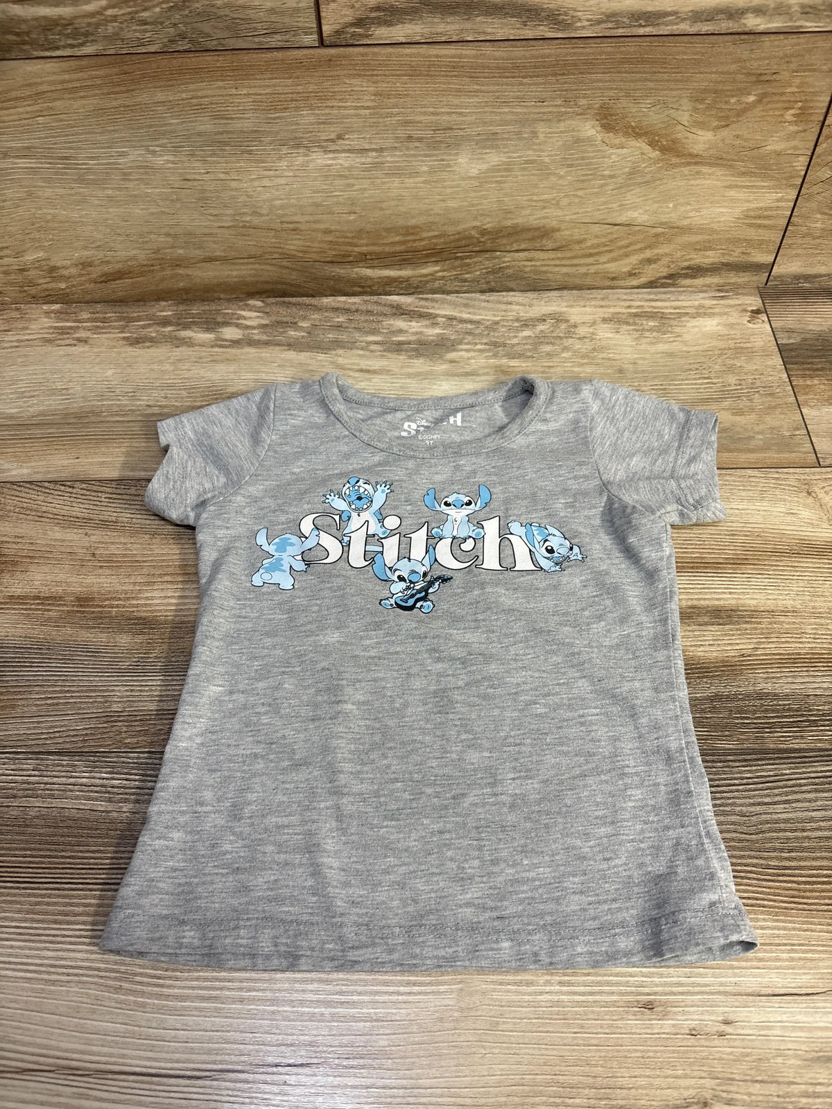 Front view of a grey Disney Stitch shirt showcasing a colorful Stitch graphic with a wood background