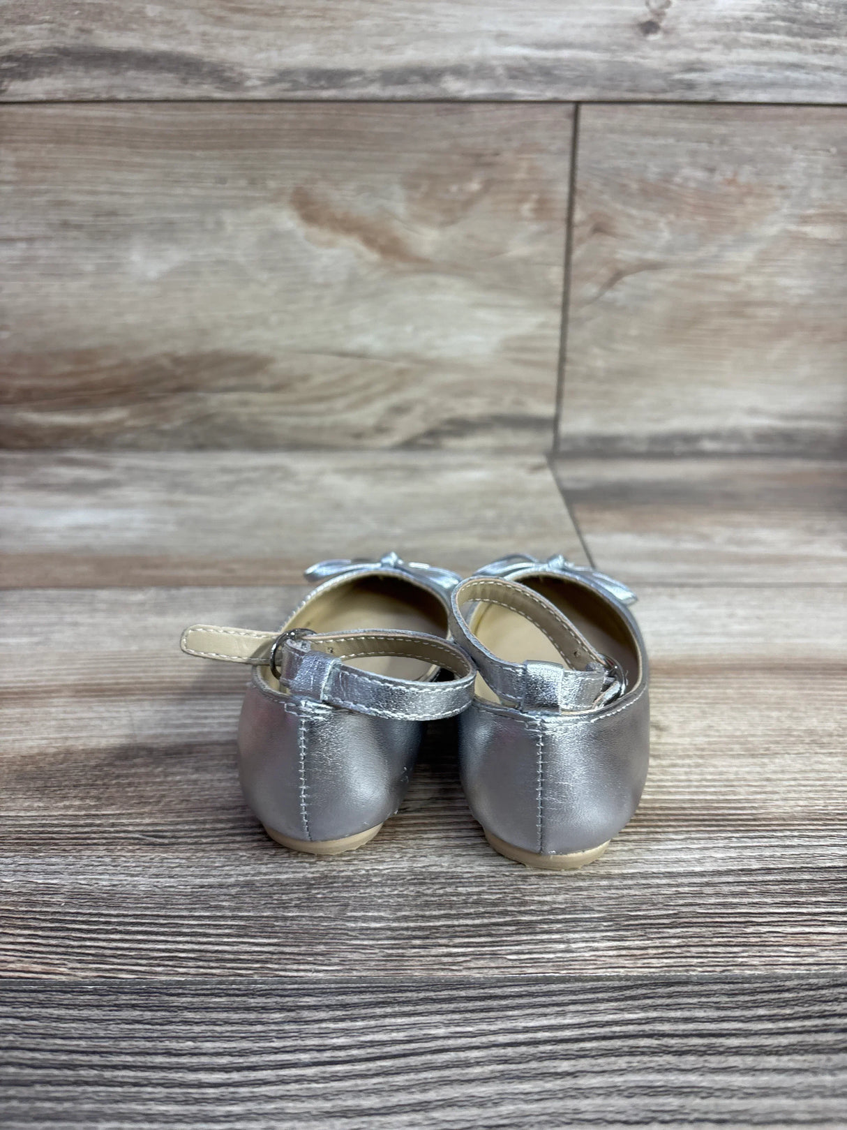 Back view of silver metallic toddler girl Mary Jane shoes with ankle straps on wooden surface