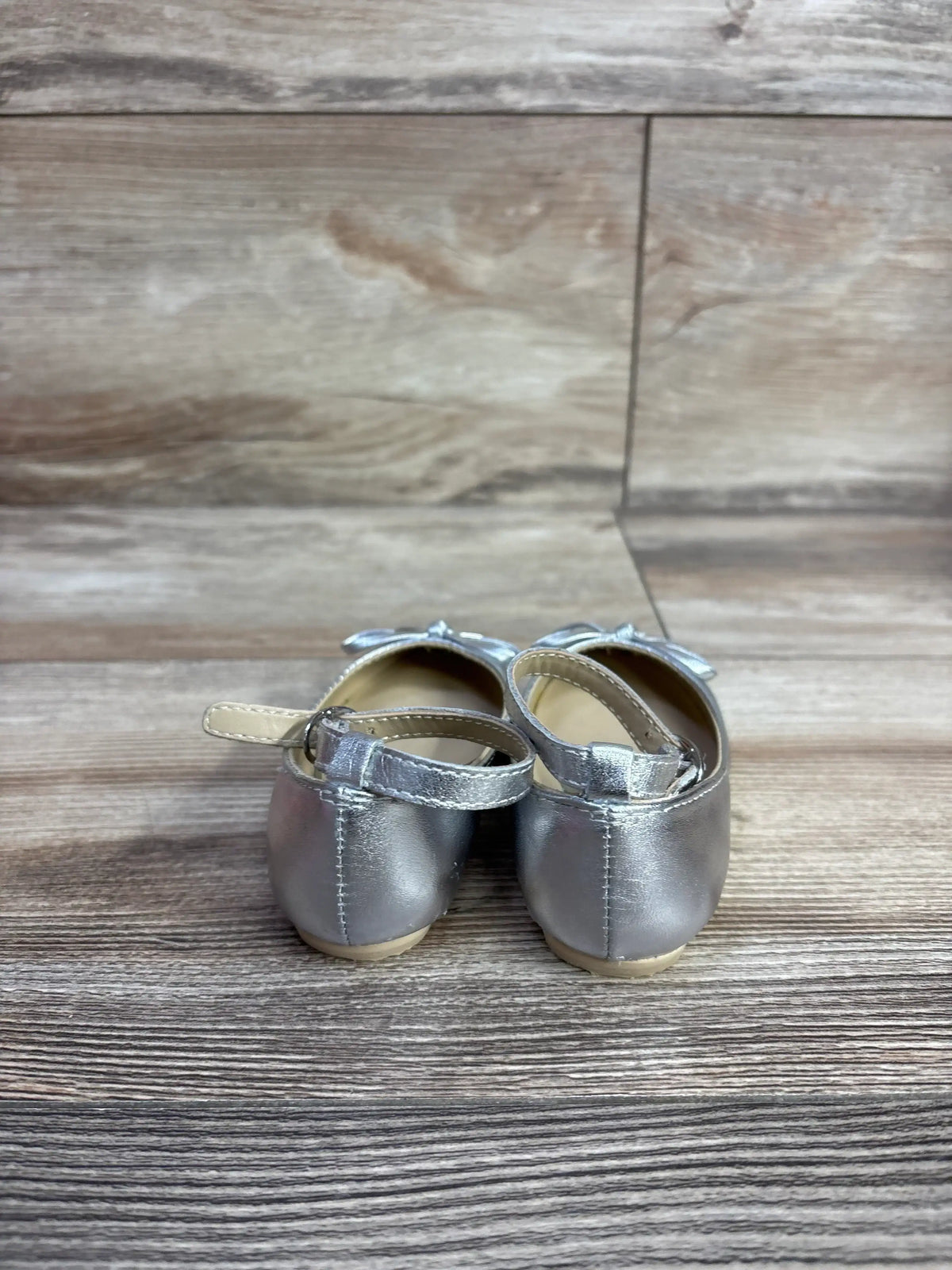 Back view of silver metallic toddler girl Mary Jane shoes with ankle straps on wooden surface