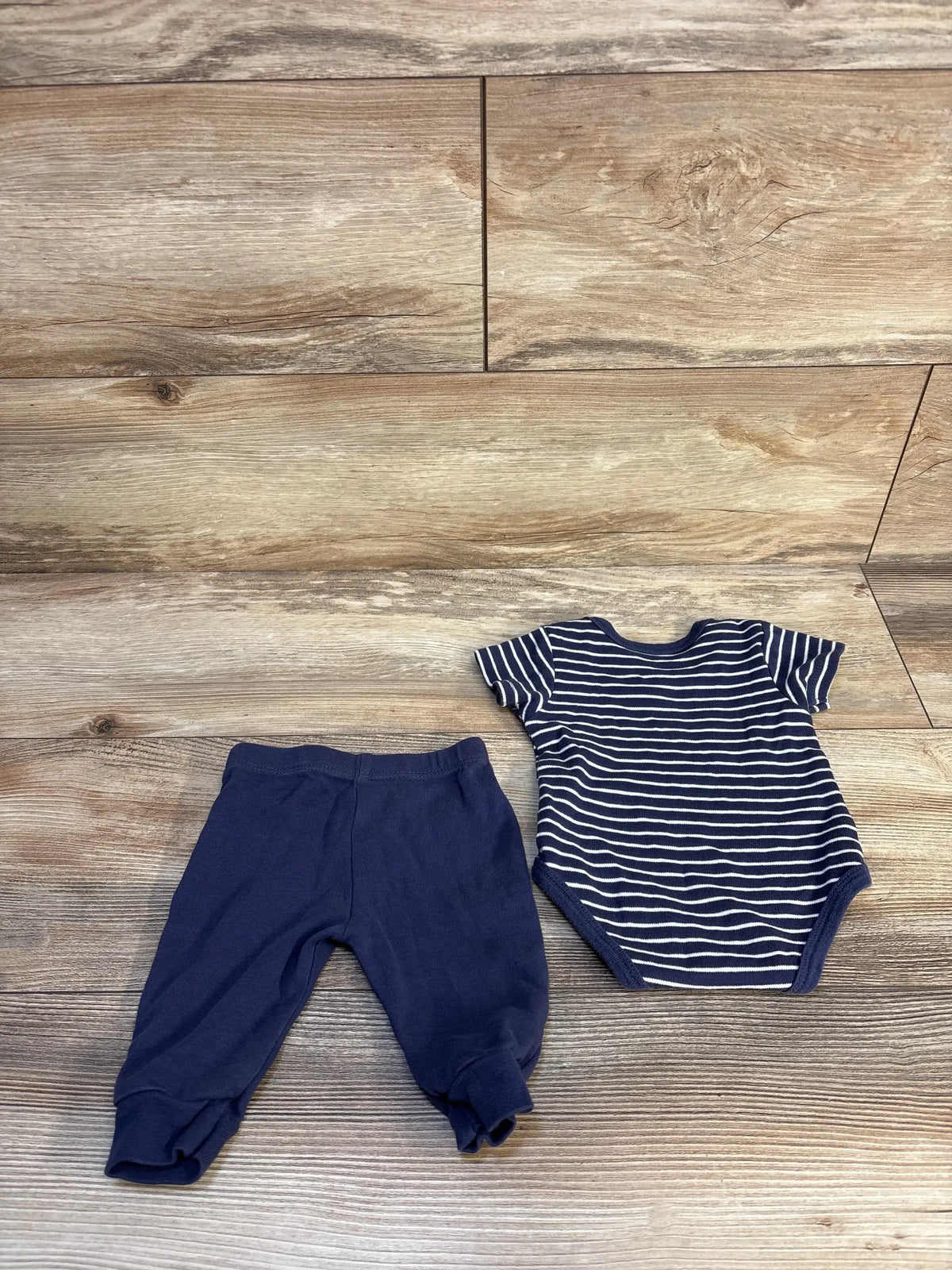 Navy blue baby pants and striped short sleeve onesie on wood background