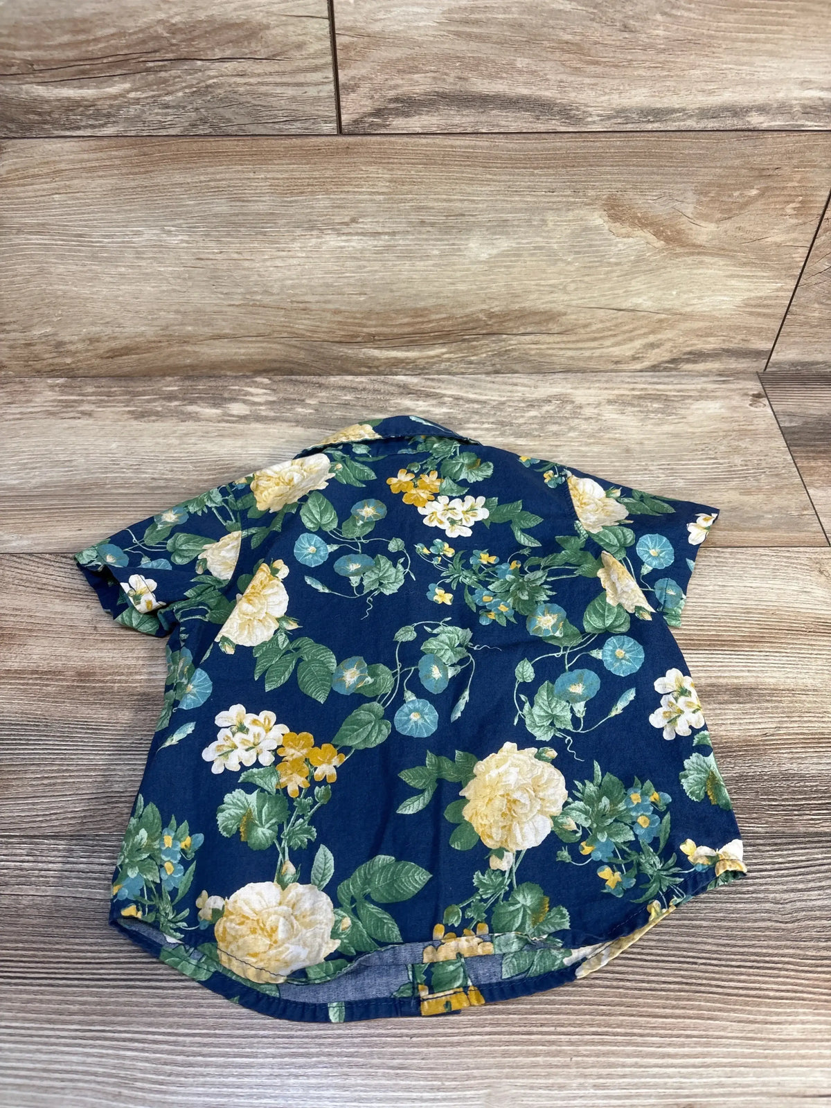 Back view of Old Navy toddler navy button-up short-sleeve shirt showcasing yellow and white floral print on wood background
