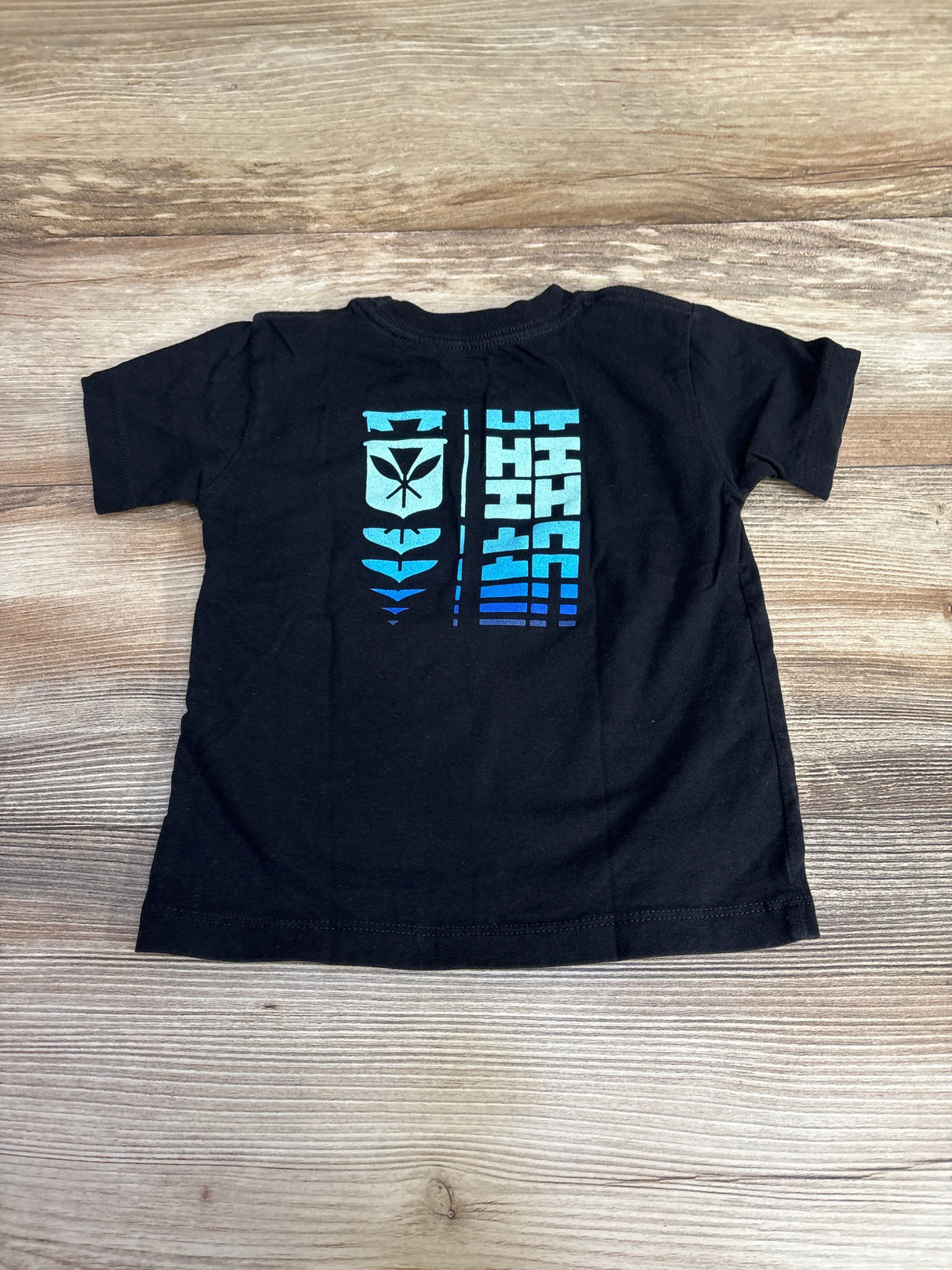 Black t-shirt with blue geometric and leaf graphic design on the back, on wood background