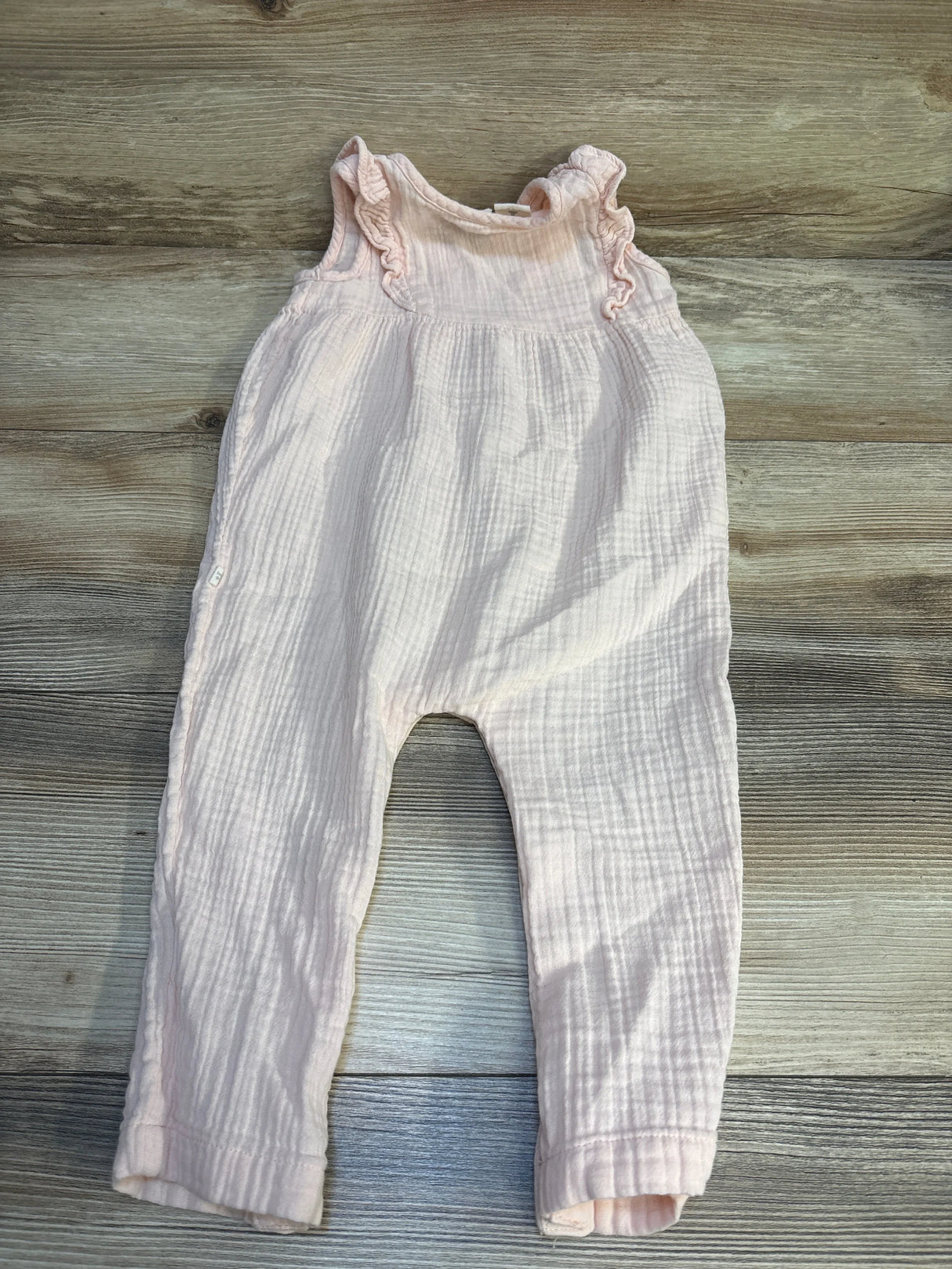 Light pink baby romper with ruffle sleeves on wood background, gently used kids clothing