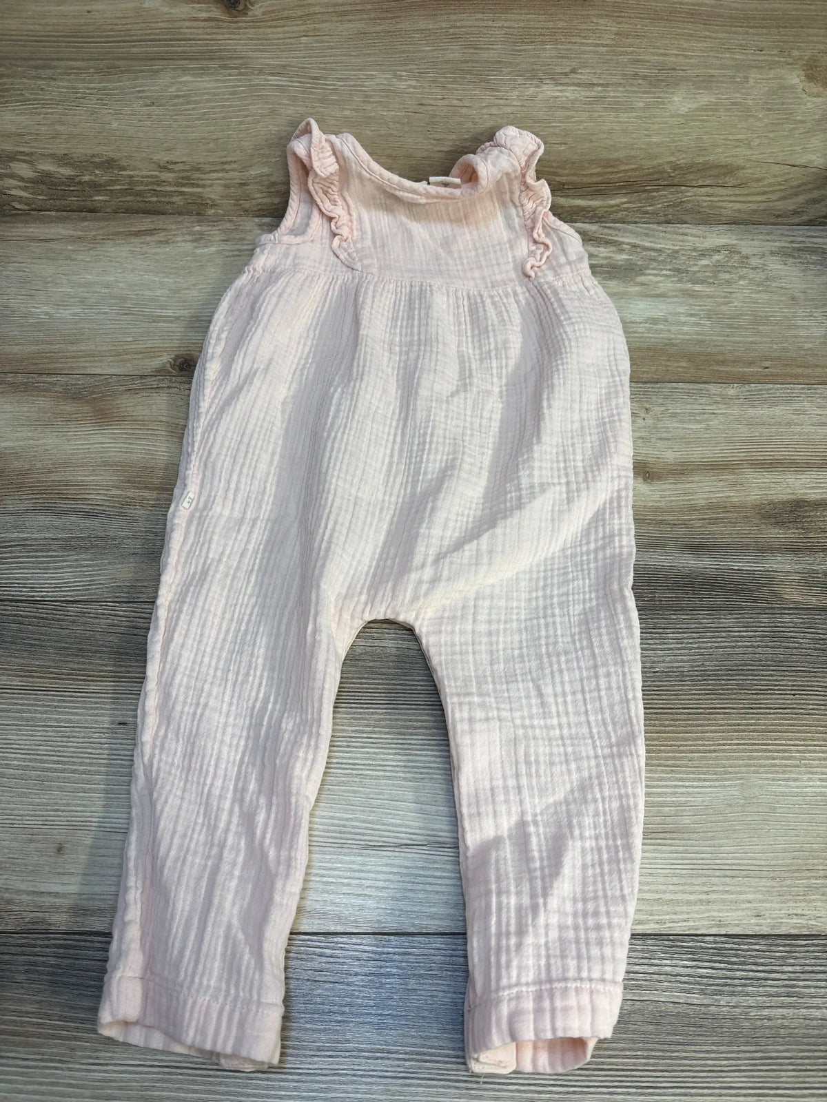Light pink baby romper with ruffle sleeves on wood background, gently used kids clothing