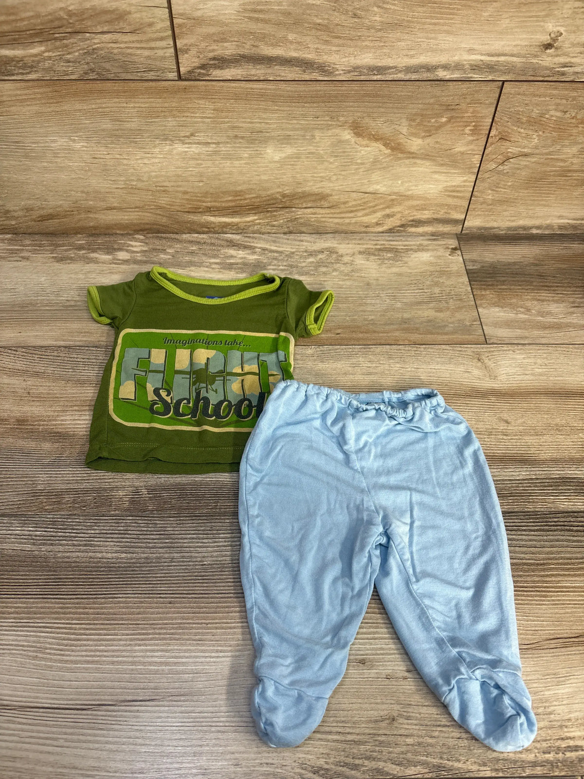 Top-down view of Kickee Pants two-piece bamboo set showing a graphic green shirt and light blue footed pants on flooring