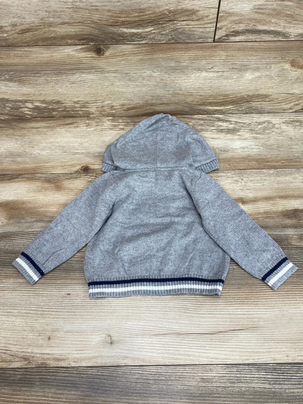 Back of grey Janie and Jack hooded baby sweater 6-12M with navy white striped cuffs and hem on wood background