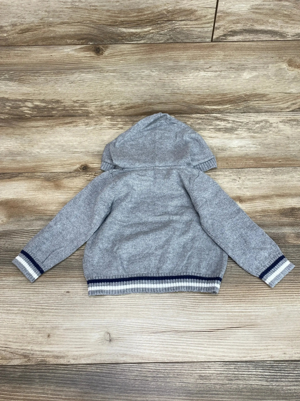 Back of grey Janie and Jack hooded baby sweater 6-12M with navy white striped cuffs and hem on wood background