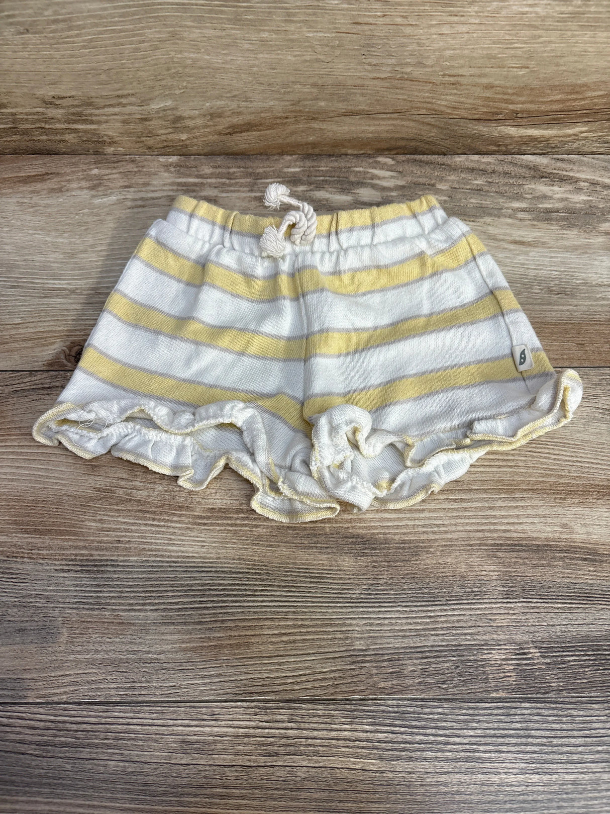 Flat lay of white and pale yellow striped toddler shorts showing elastic drawstring waist and ruffled hem on wood background