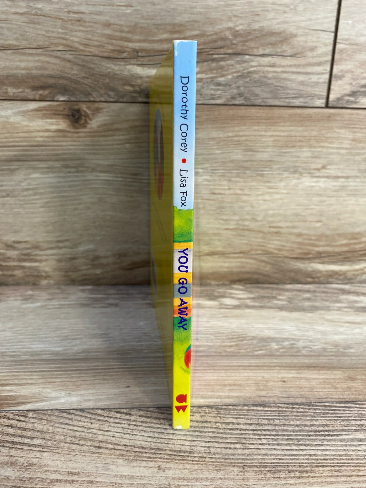 Spine view of You Go Away board book showing title on yellow spine with wooden tabletop background