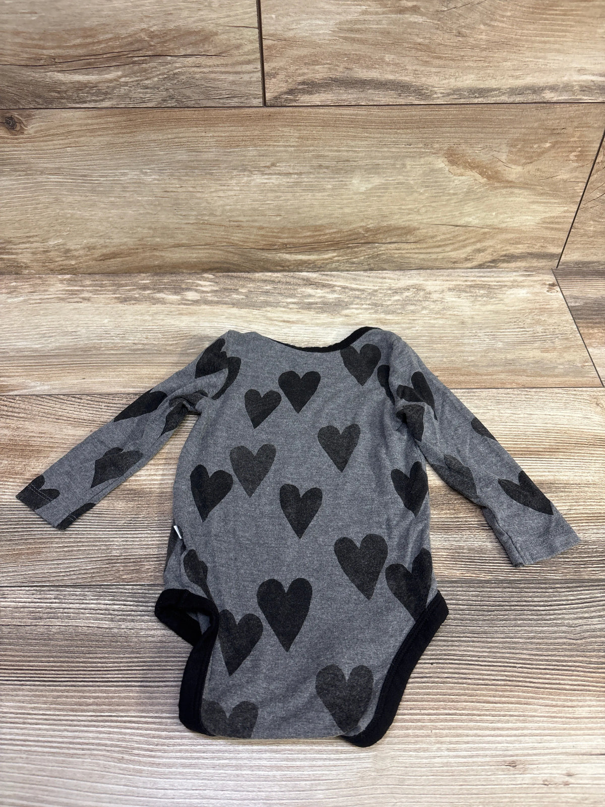 Front view of Play by Little Sleepies grey long-sleeve bodysuit with black heart pattern on a wood-look floor