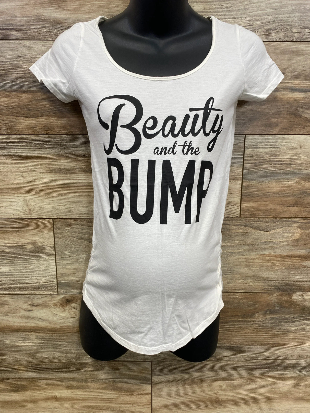 White maternity t-shirt with black text reading Beauty and the Bump on black mannequin against wood background