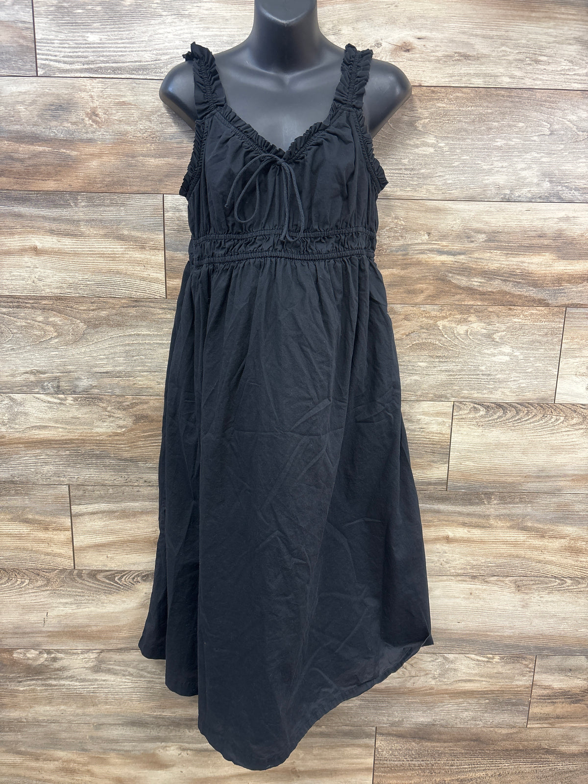 Front view of Old Navy black maternity sleeveless dress showcasing ruched straps and tie front with wood plank background