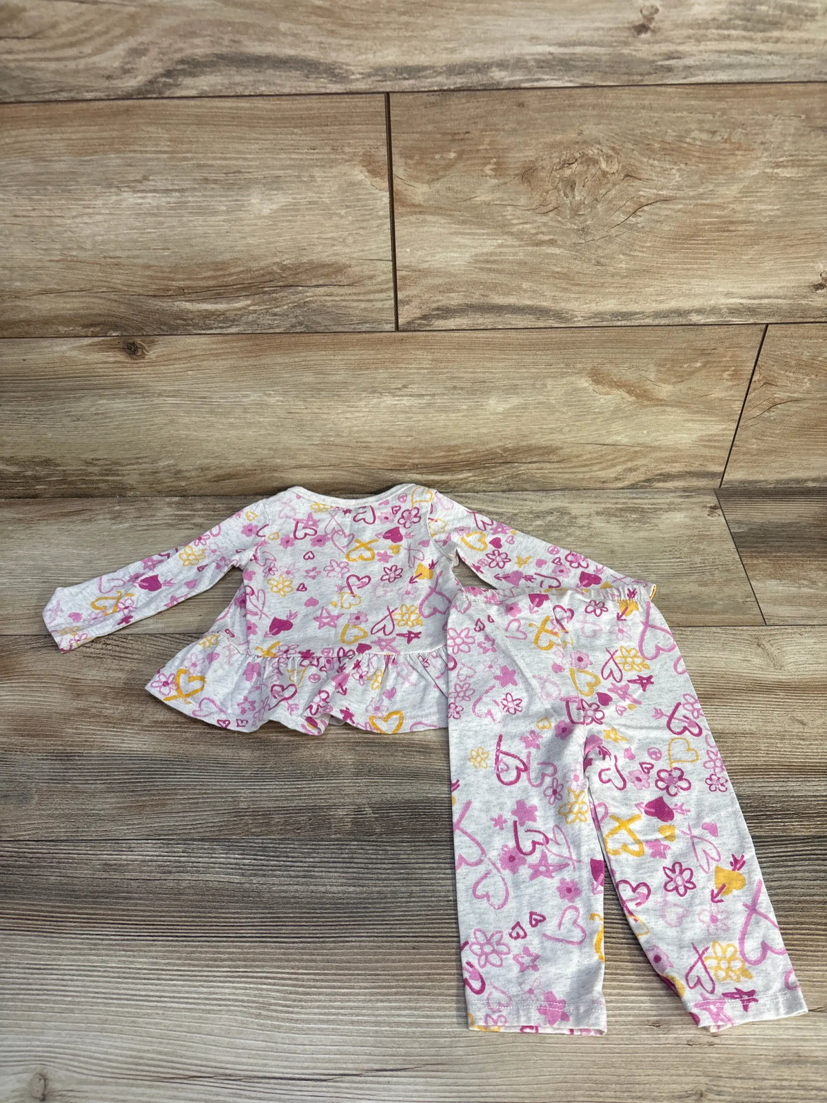 Flat lay of gray two-piece peplum top and bottoms set showcasing ruffled detail with pink and yellow pattern on wood flooring