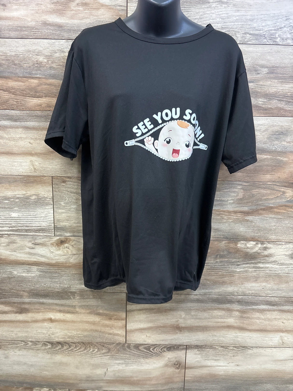Front view of black maternity T-shirt with ‘See You Soon’ zipper-baby graphic on mannequin against wood background