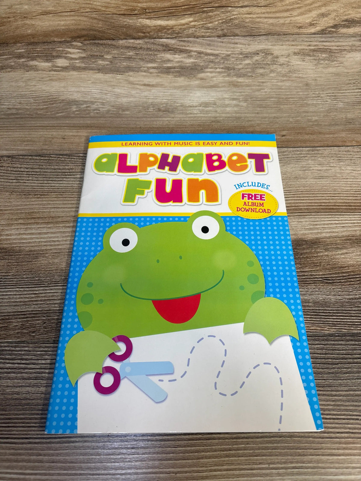 Front view of Bendon Alphabet Fun Activity Book with frog artwork and tracing activity on wooden surface