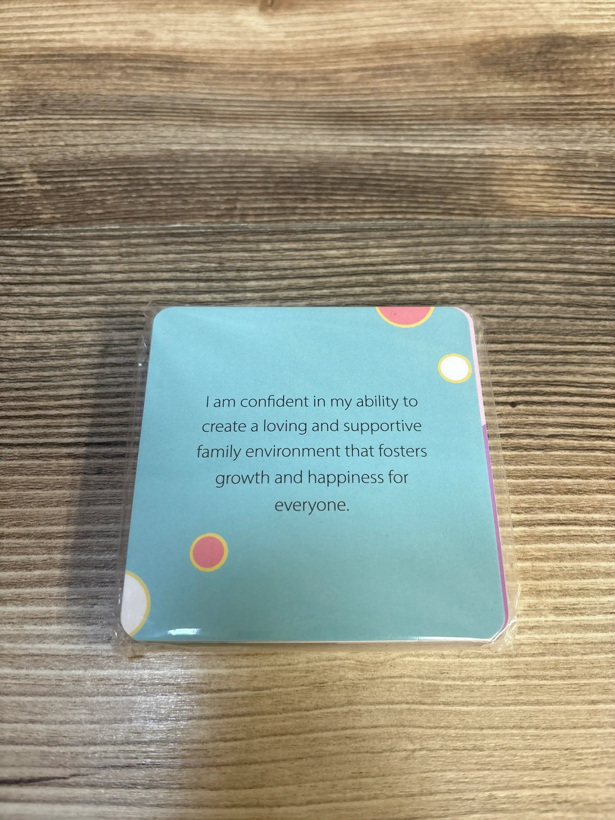 Top view of pregnancy affirmation card reading I am confident, teal card in sealed sleeve on wood background