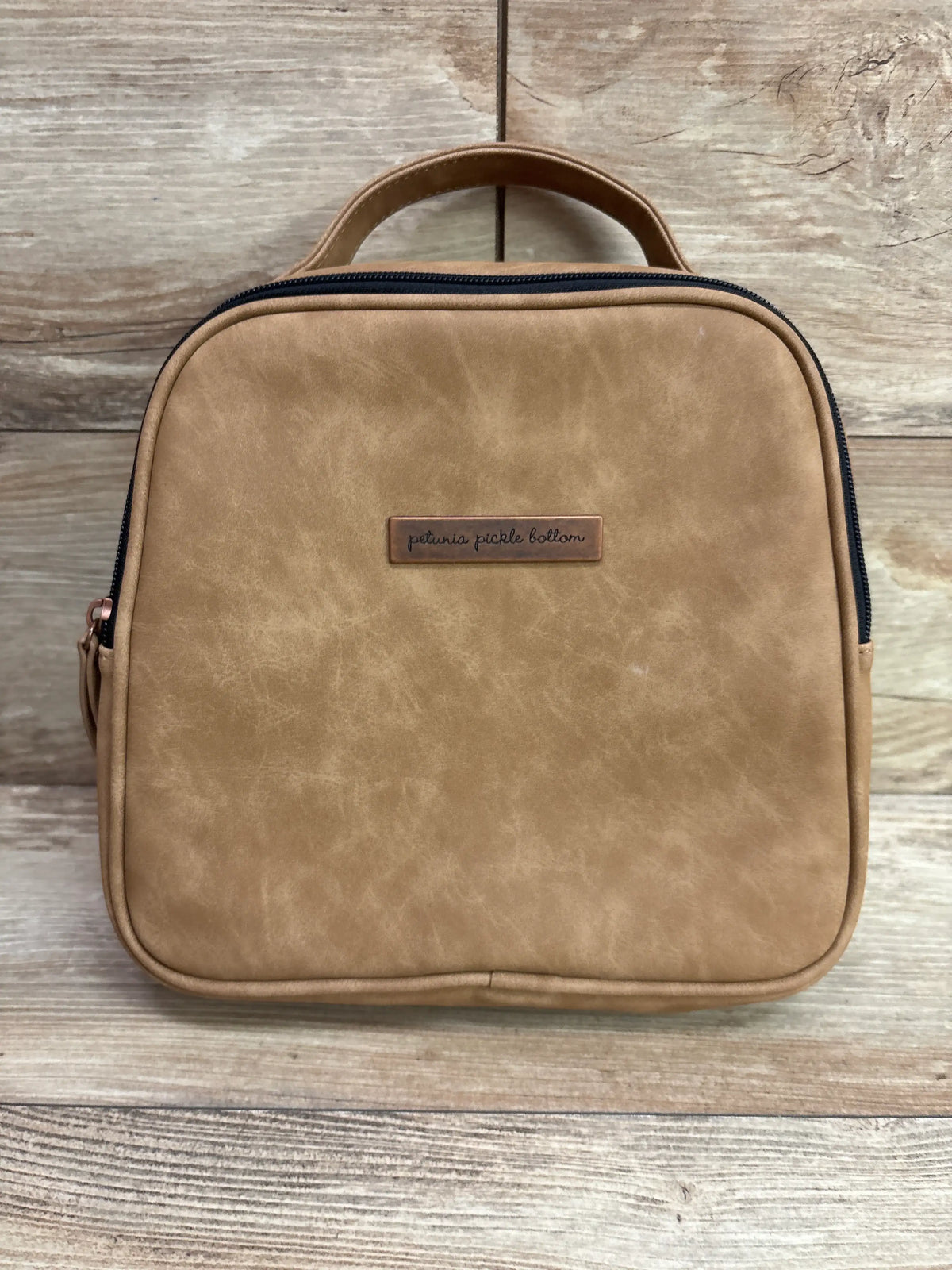 Front view of Petunia Pickle Bottom Tandem Bottle and Lunch Tote showcasing brown exterior, top handle, and zippered closure with wood background
