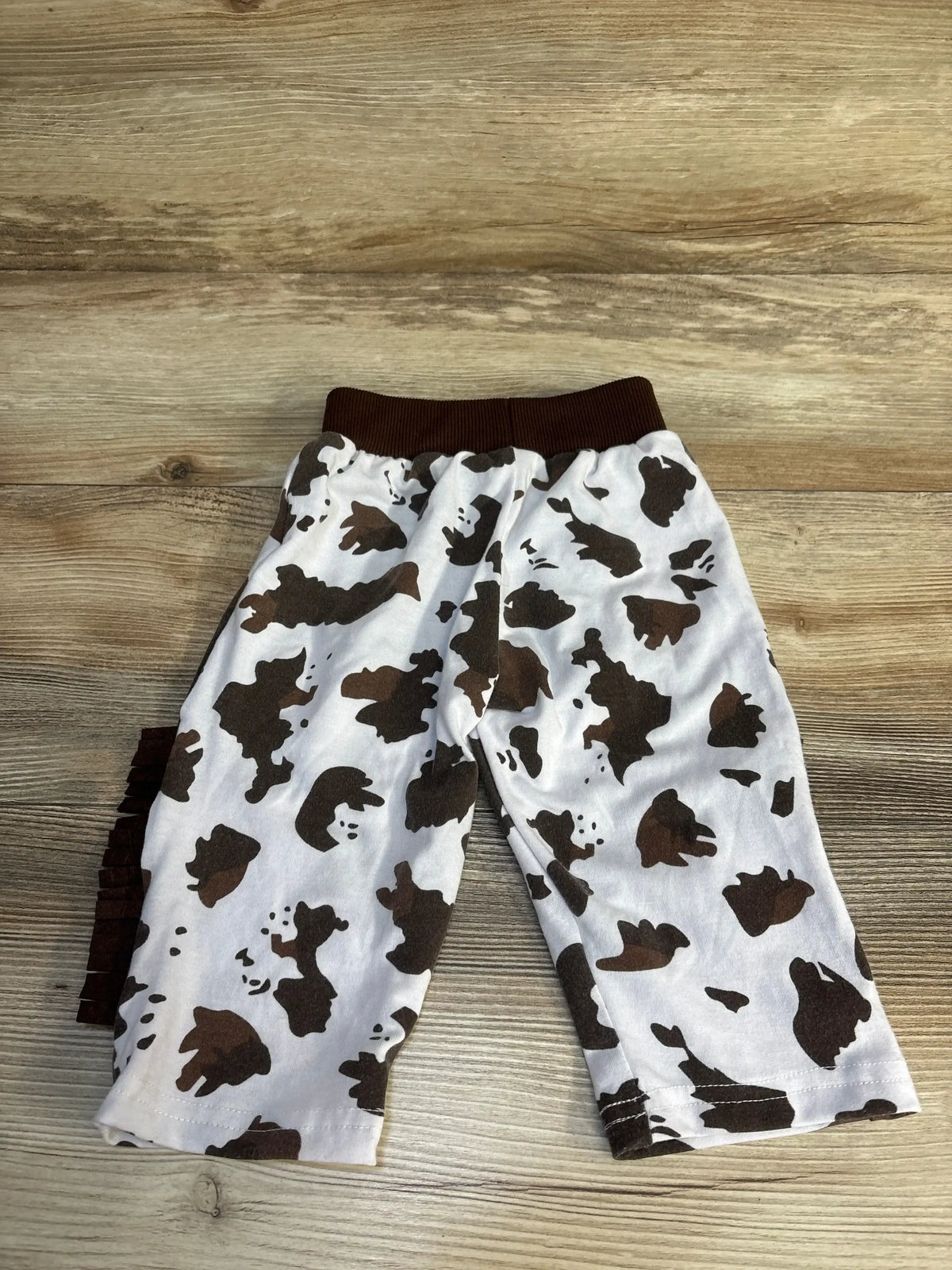 Kids cow print pants with brown waistband, soft cotton baby clothing on wood floor