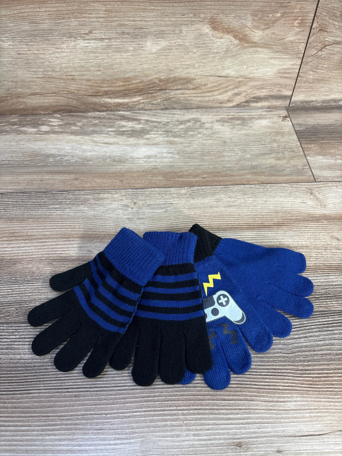 Top view of Toby and Me two pack baby gloves showing solid blue and blue and black striped pairs on a wood grain surface