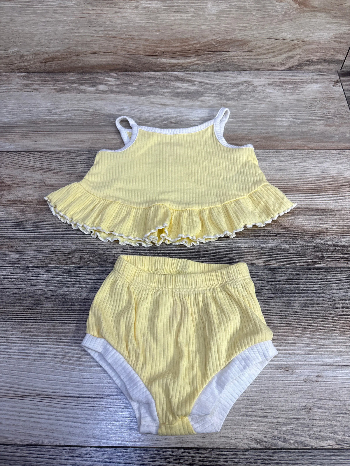 Top-down view of yellow ribbed tank top and bloomers set showcasing peplum ruffle and white trim on wood-grain background