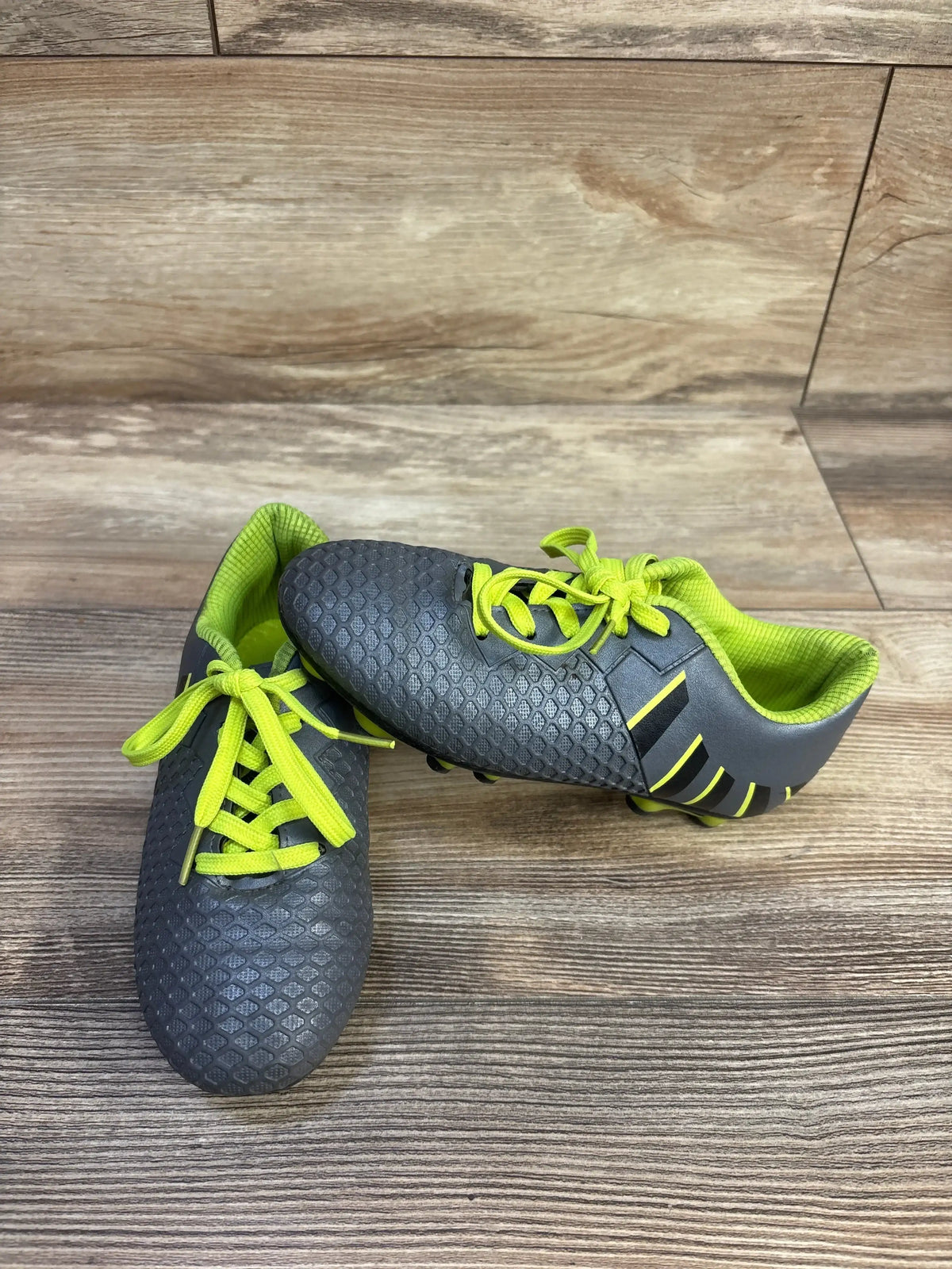 Angled front view of Hawkwell athletic soccer cleats size 12C showcasing grey textured upper with neon yellow laces and lining on wood floor background