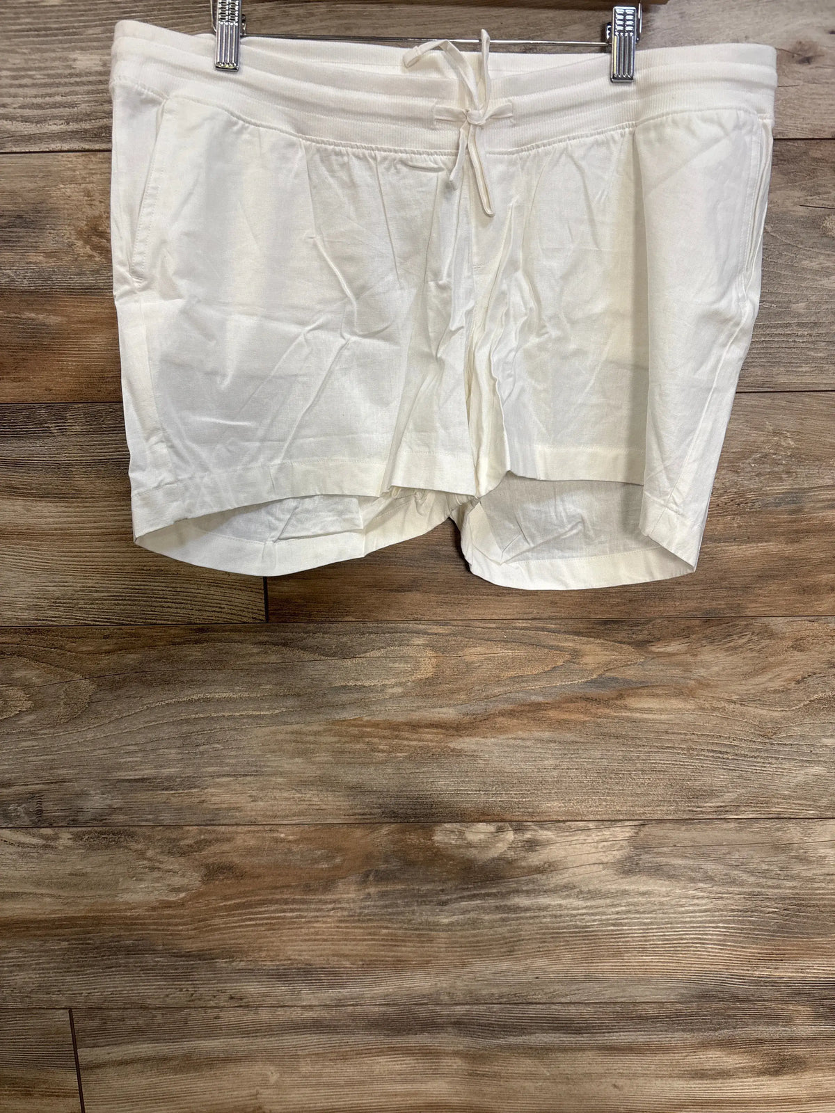 Front view of white Gap maternity linen blend shorts showcasing under belly drawcord waist and front slant pockets on wood