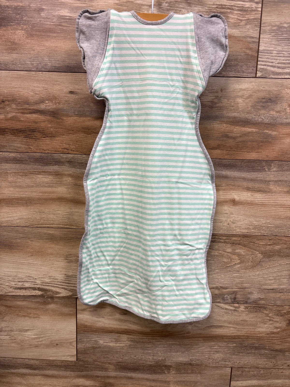 Front view of Love To Dream Swaddle UP in teal stripes, size L (6-12 months) showing winged arm openings on wooden background