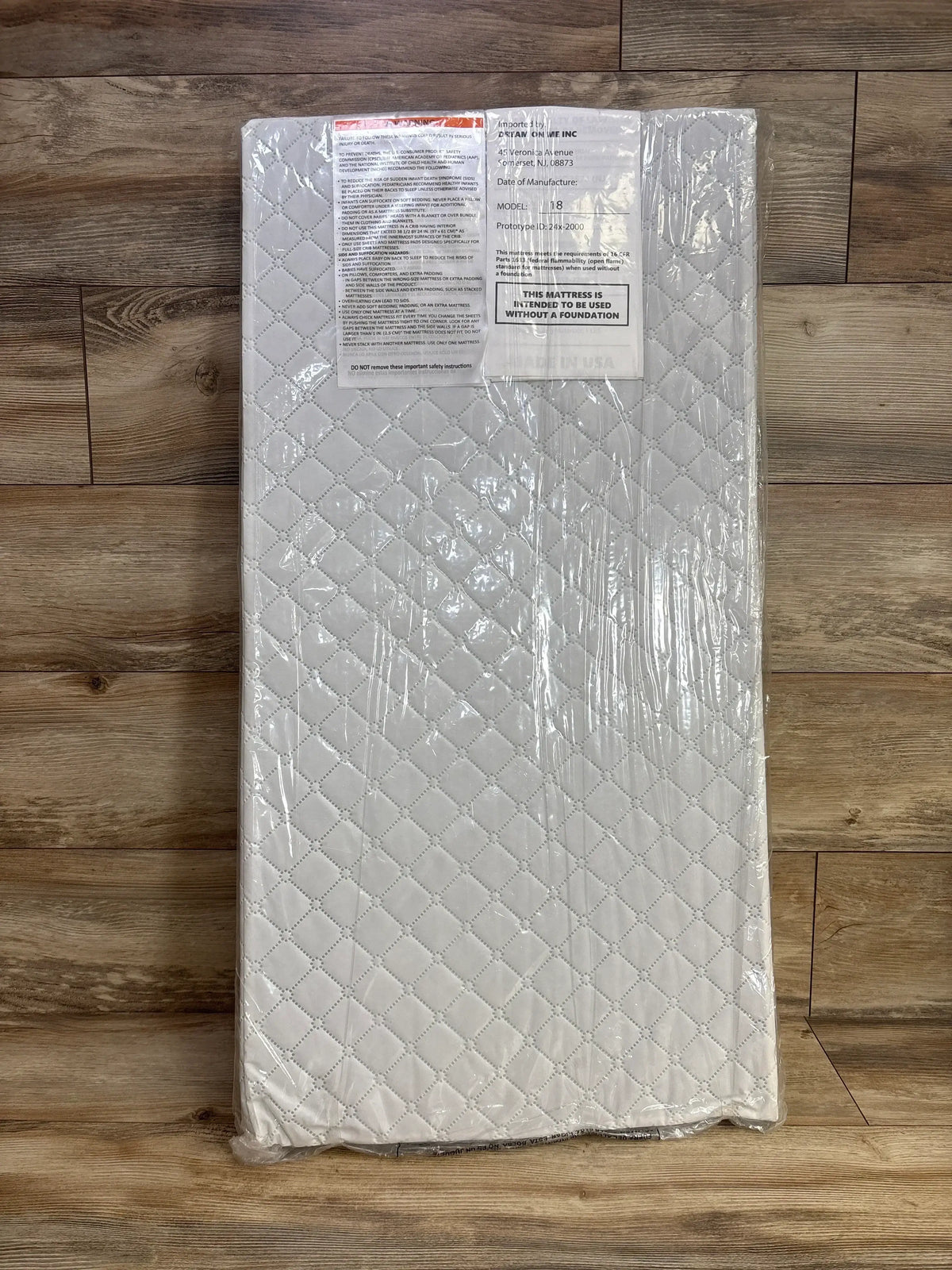 Top-down view of Dream On Me cradle mattress 36 x 18 x 2 in showing white quilted cover in clear plastic on wooden floor
