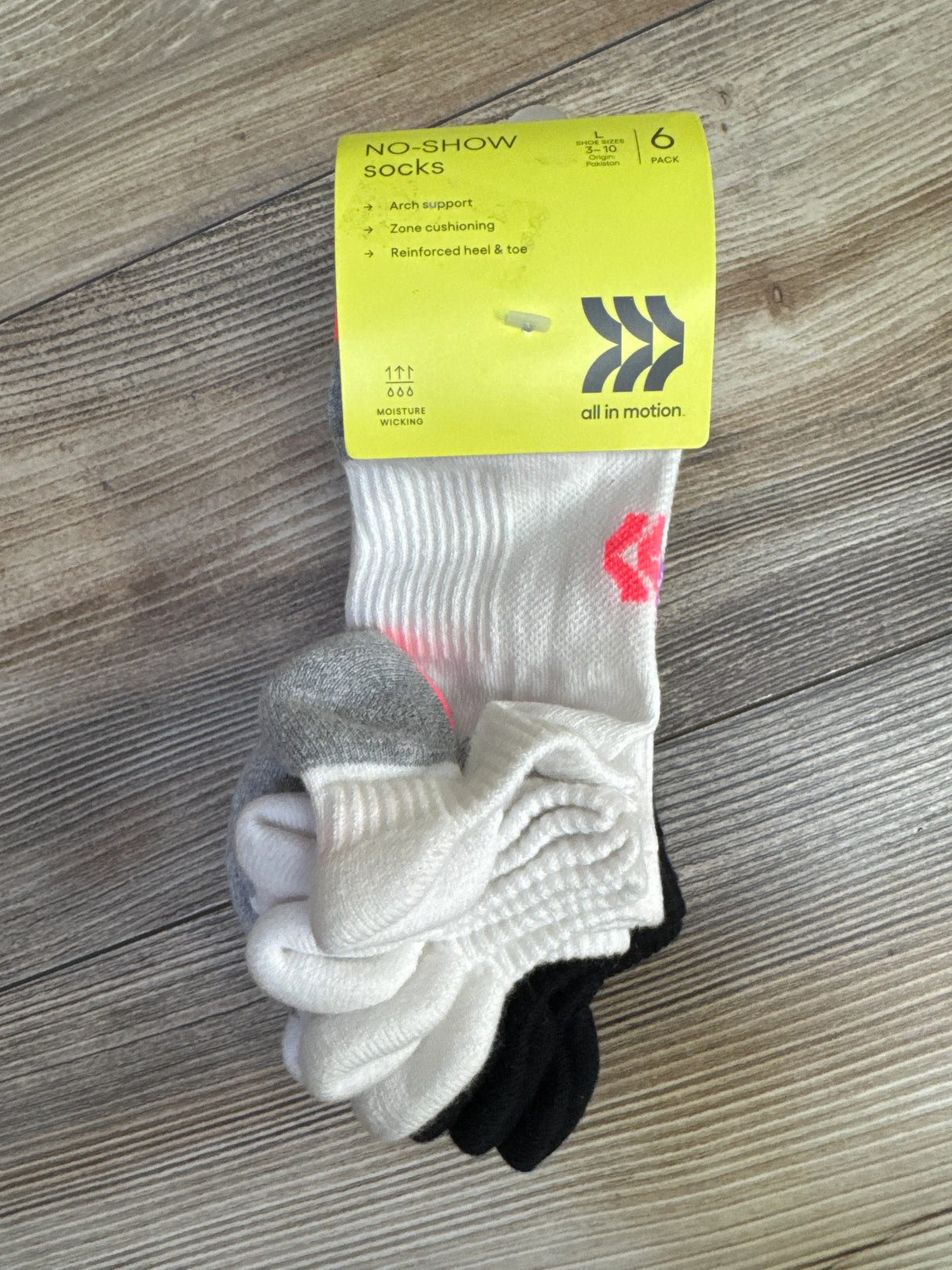Top view of All in Motion no-show socks 6-pack (3-10Y) showing white, gray and black pairs with yellow label on wood floor
