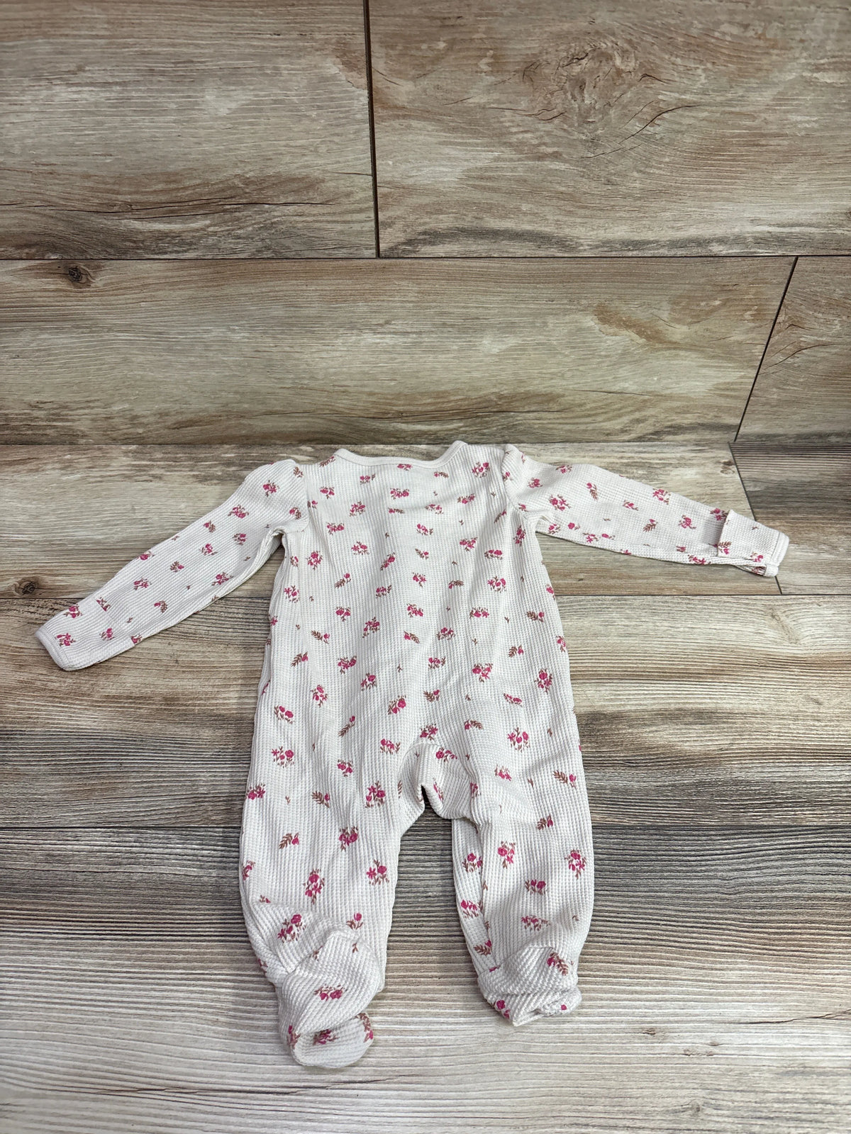 Top view of Carters beige waffle knit sleeper showcasing long sleeves, footed legs, and pink floral print on wood flooring