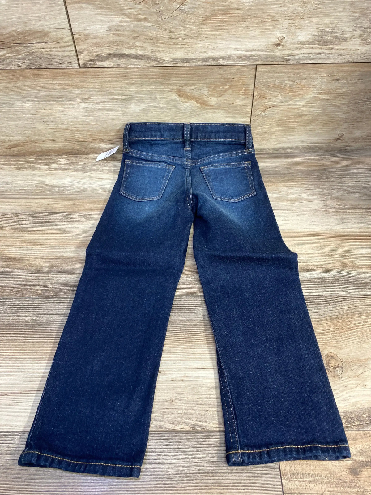 Child's dark blue denim jeans with back pockets on wooden floor background