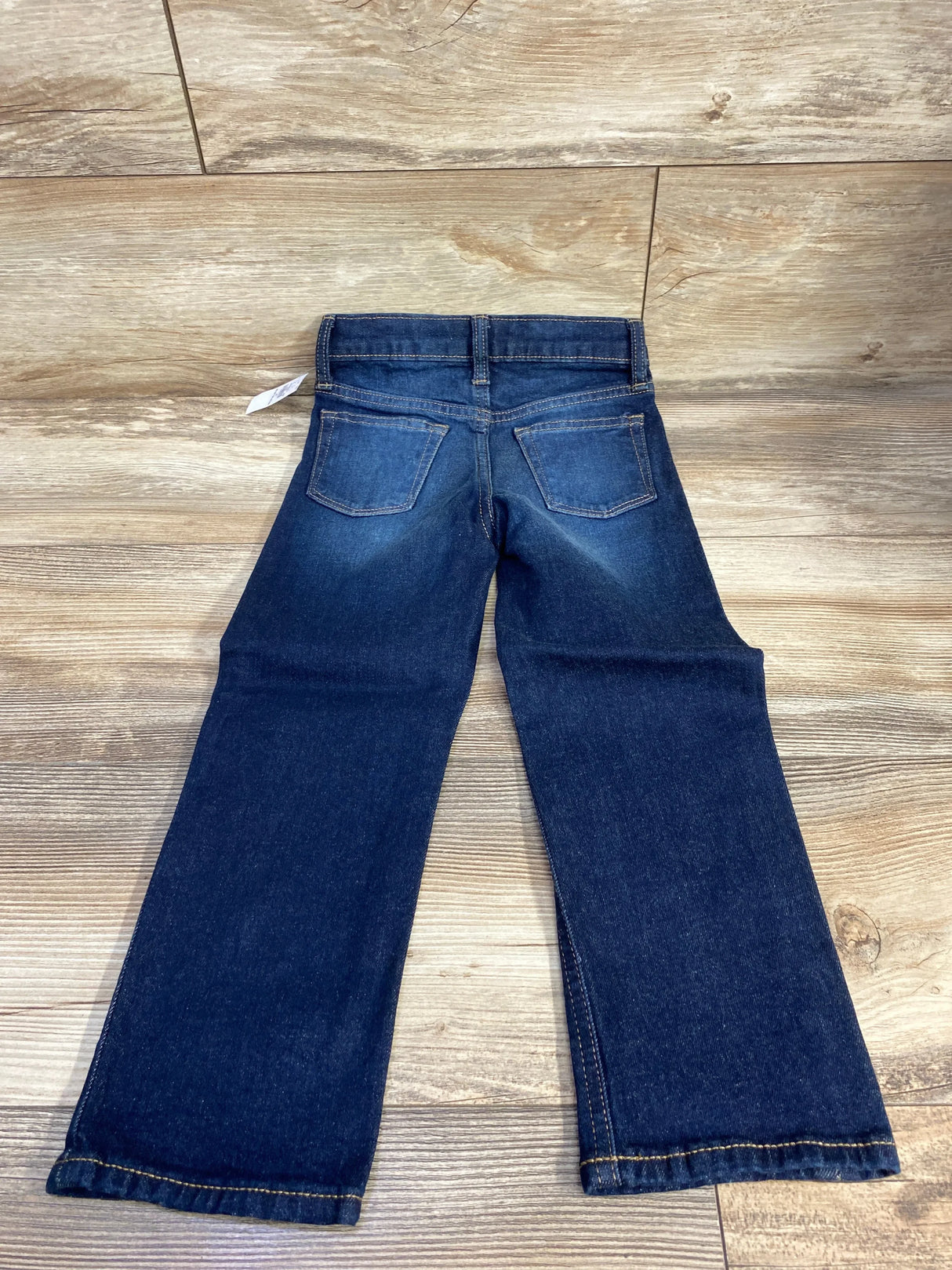 Child's dark blue denim jeans with back pockets on wooden floor background