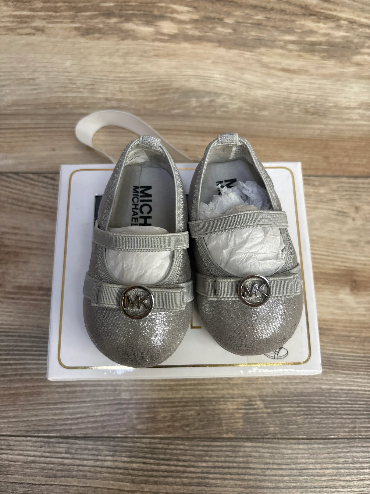 Top view of Michael Kors Rover Lux baby shoes in silver glitter, size 2C, showing elastic strap and gold MK logo on white box